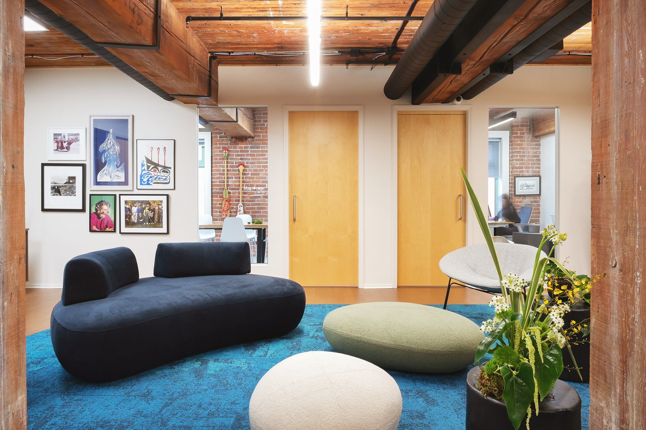 Lounge with a curved navy sofa and boulder-form poufs facing the maple meeting room doors