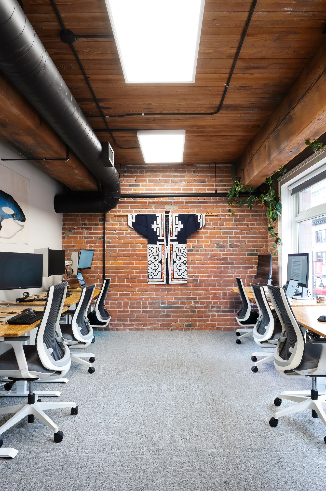 Open workspace with live-edge desks and an embroidered robe displayed on the brick wall
