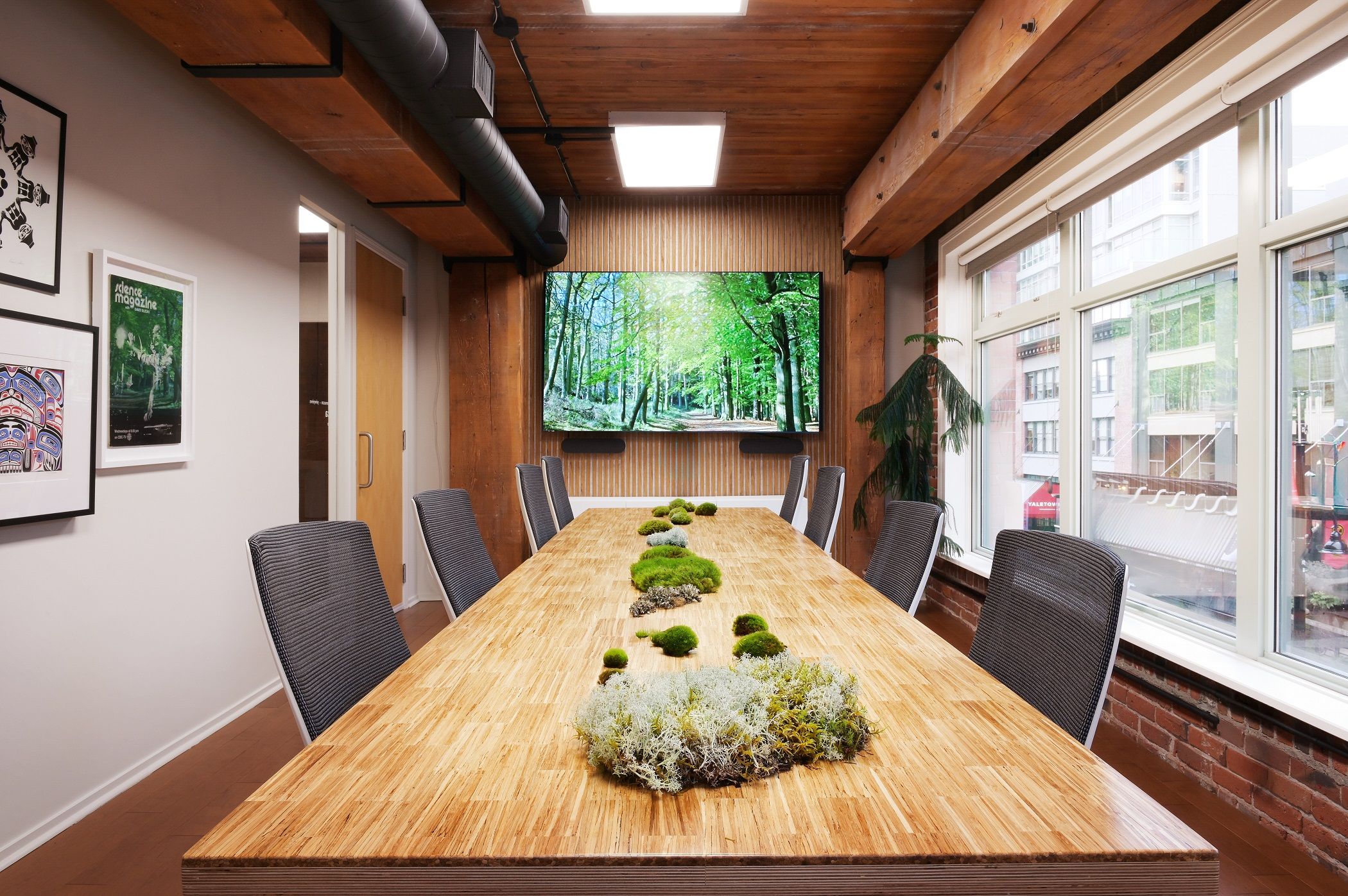 Butcher-block boardroom table with a moss and lichen runner beneath the forest display