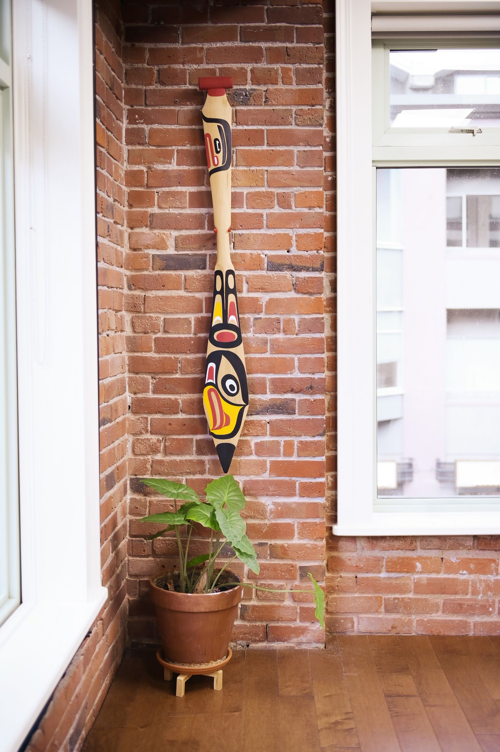 Carved paddle mounted on exposed brick between two windows, with a potted plant below