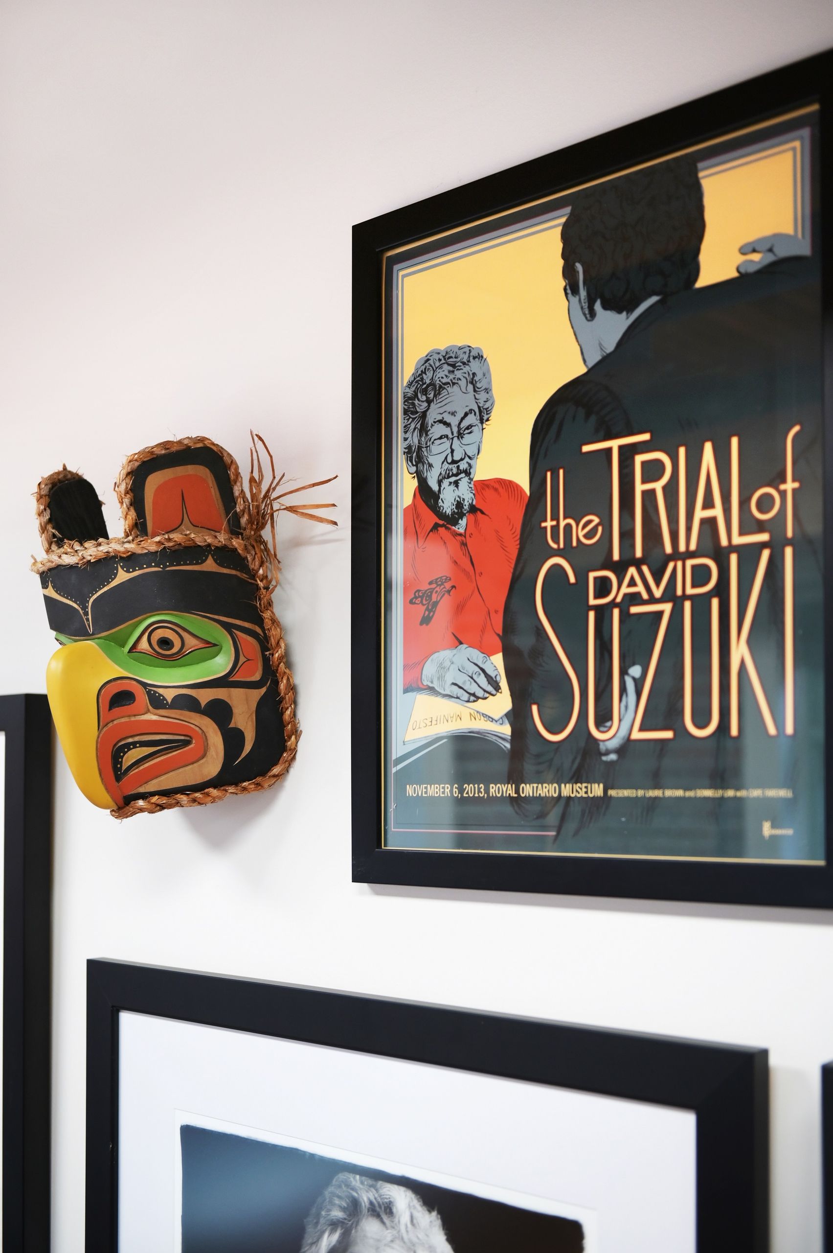 Carved cedar mask beside a framed poster for The Trial of David Suzuki