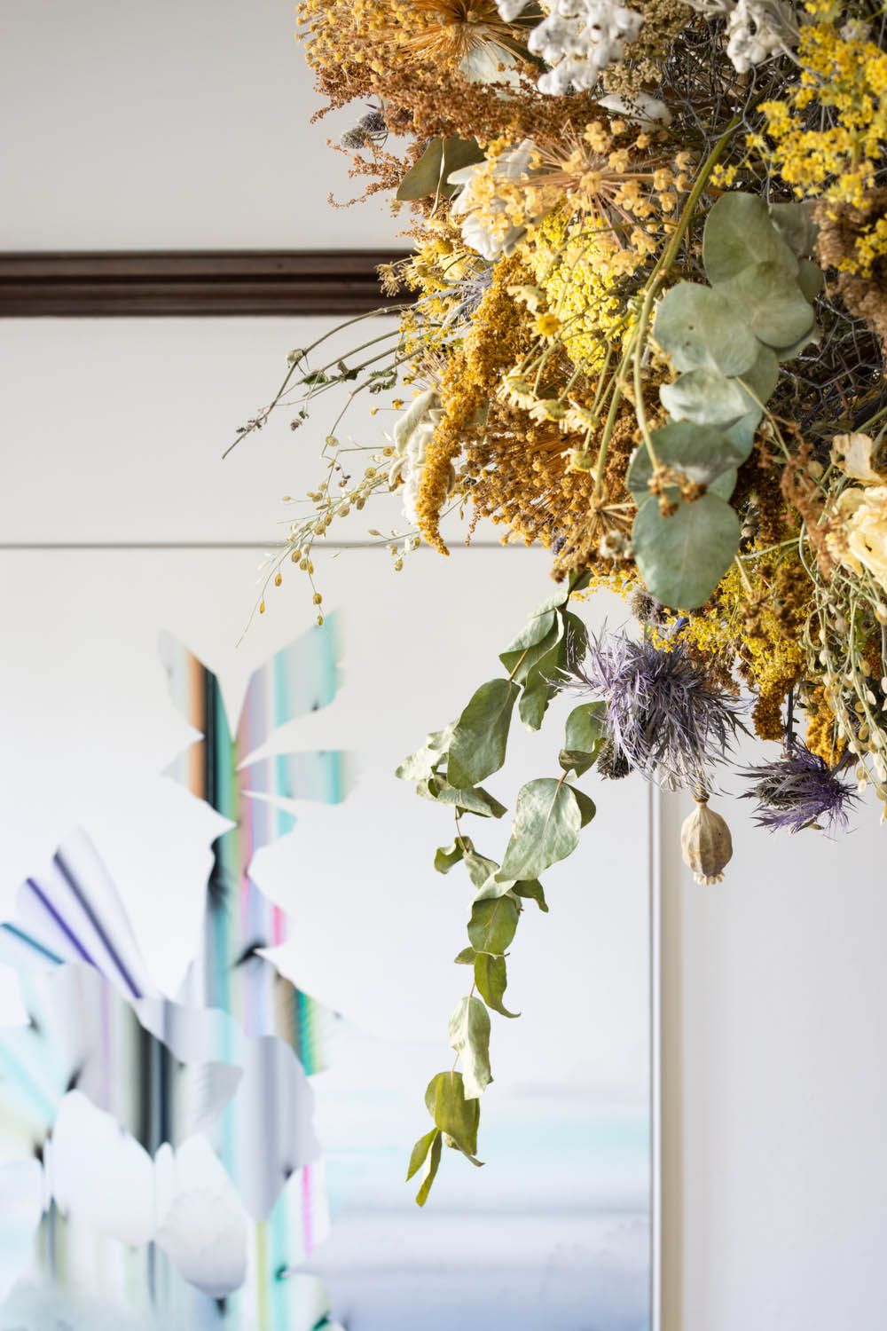 Dried yarrow, eucalyptus and poppy pods hanging in front of a pale abstract canvas