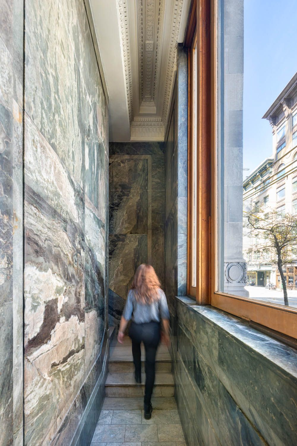 Marble-lined stair to the office, lit by the tall heritage window onto Gastown