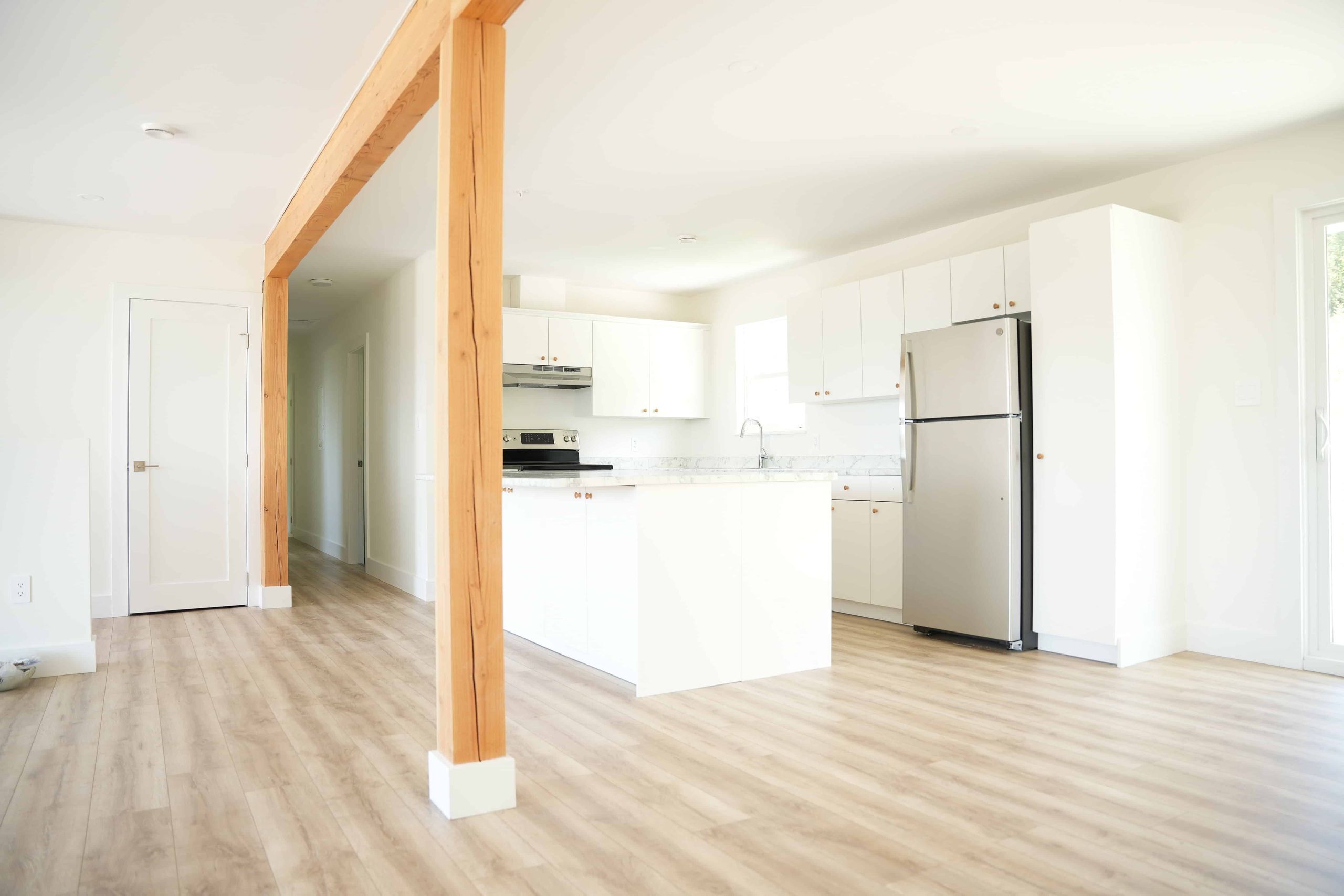 Open-plan kitchen and living area with white cabinetry and an exposed fir post in a completed home