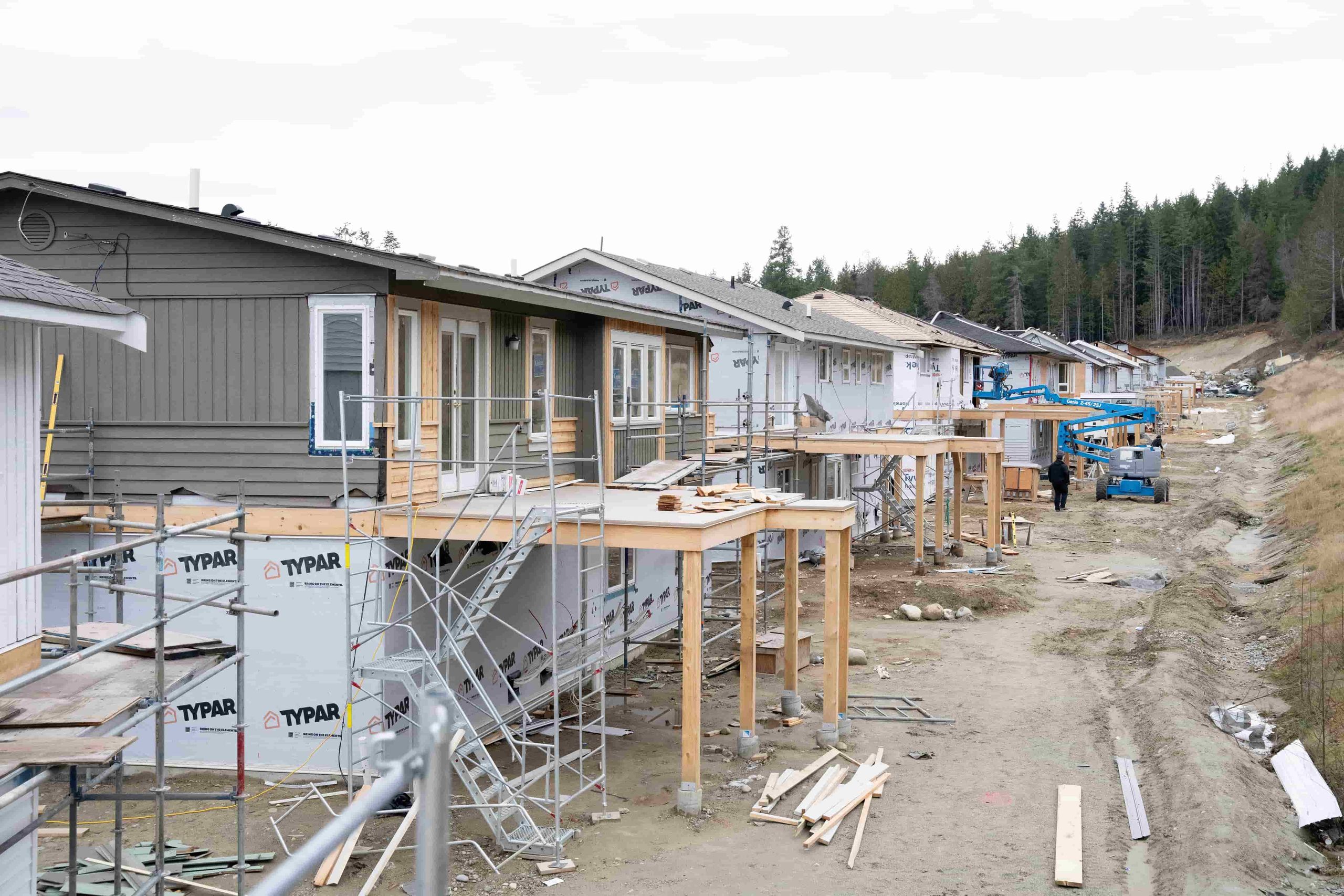 Homes under construction with scaffolding and new decks being framed along the subdivision road