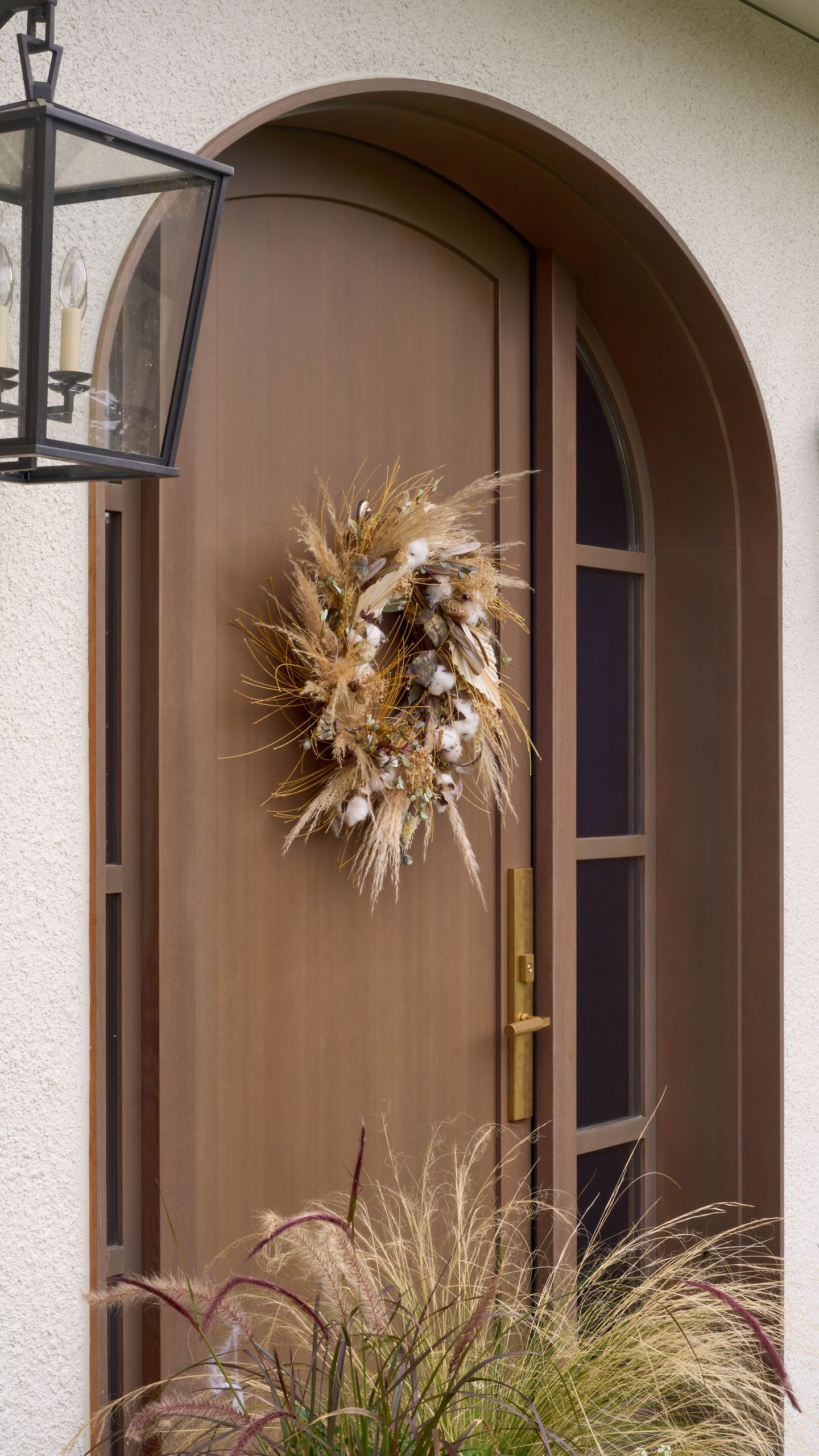 Arched mahogany front door with a dried wreath of pampas, cotton and eucalyptus