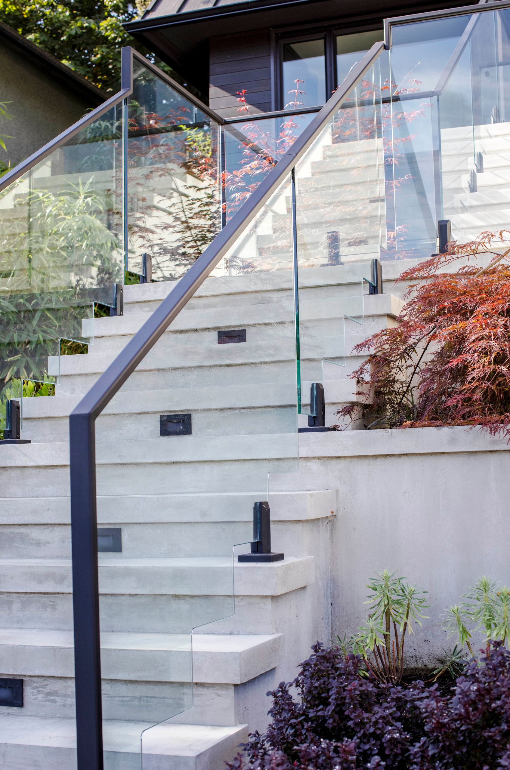 Recessed step lights set into the concrete treads beside the glass balustrade
