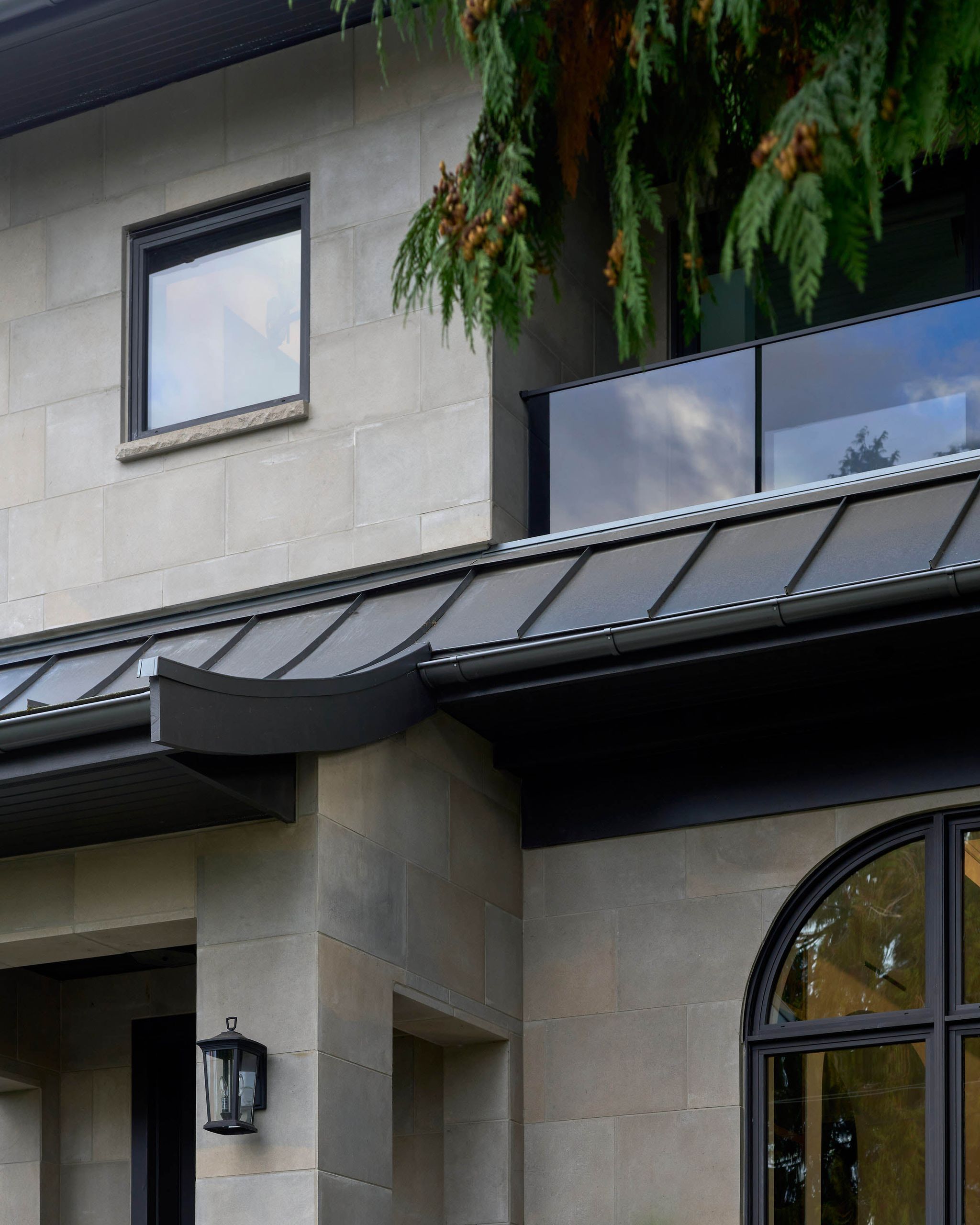 Detail of the curved metal roof edge against limestone ashlar and the glass balcony