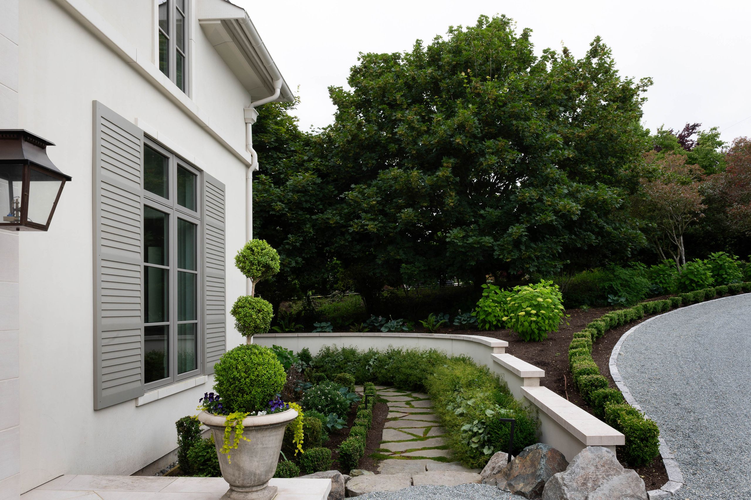 Flagstone path and curved limestone wall leading past the shuttered windows
