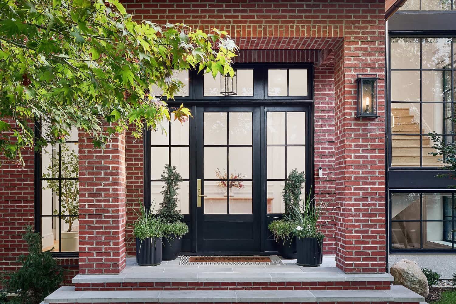 Front entry with a black glazed door, transom and sidelights set into a brick surround
