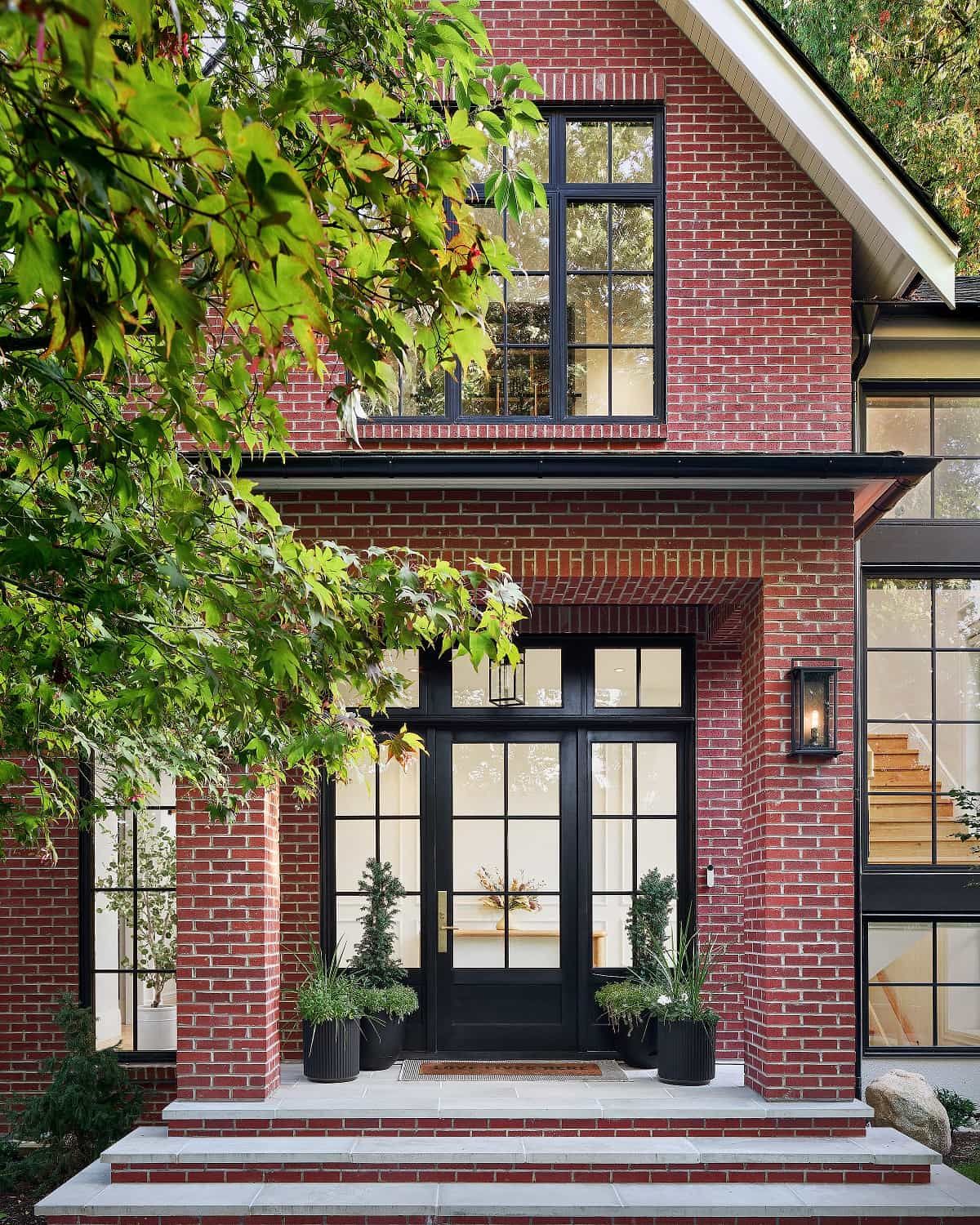 Entry and steeply pitched brick gable seen through Japanese maple foliage