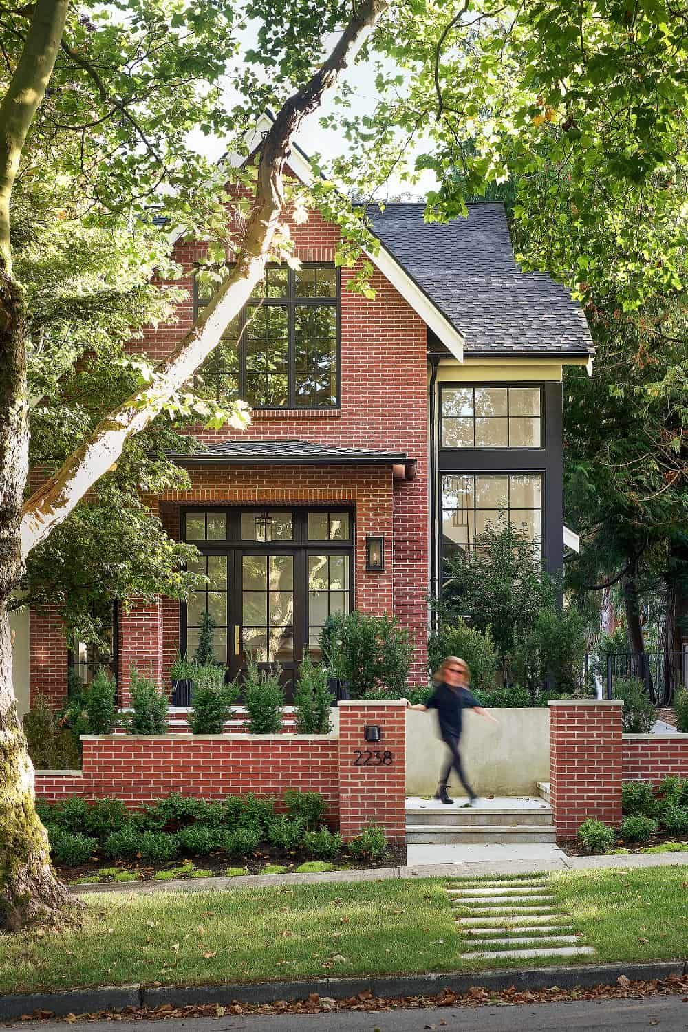 A passer-by on the sidewalk beside the brick garden wall and street-facing entry