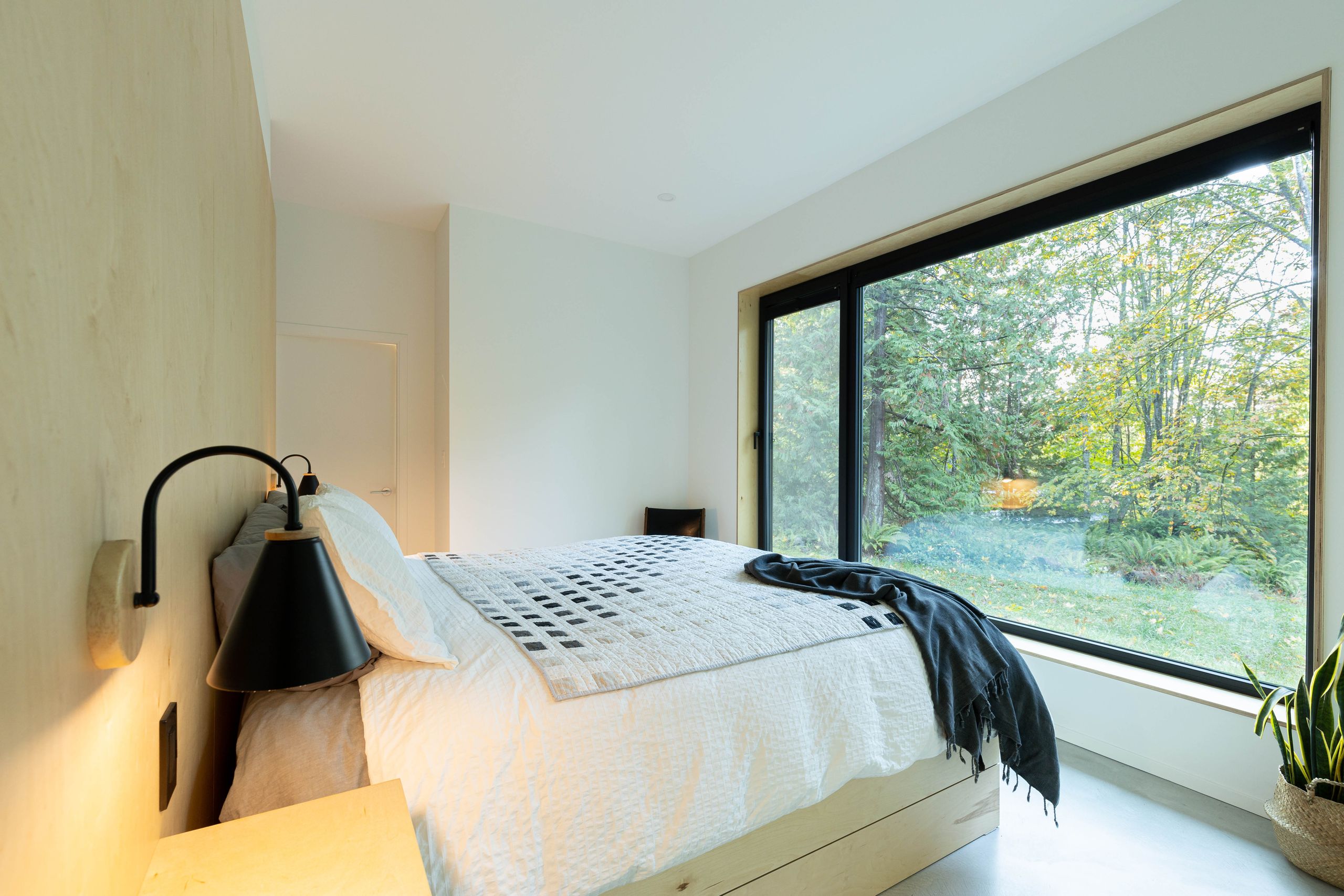 Bedroom with a birch plywood feature wall and a picture window onto the forest