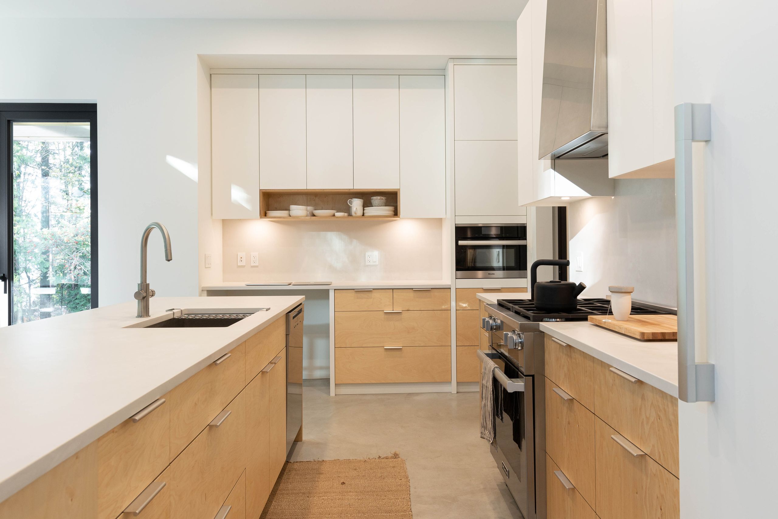 Kitchen with birch plywood cabinetry, white uppers and an open shelf of pale ceramics
