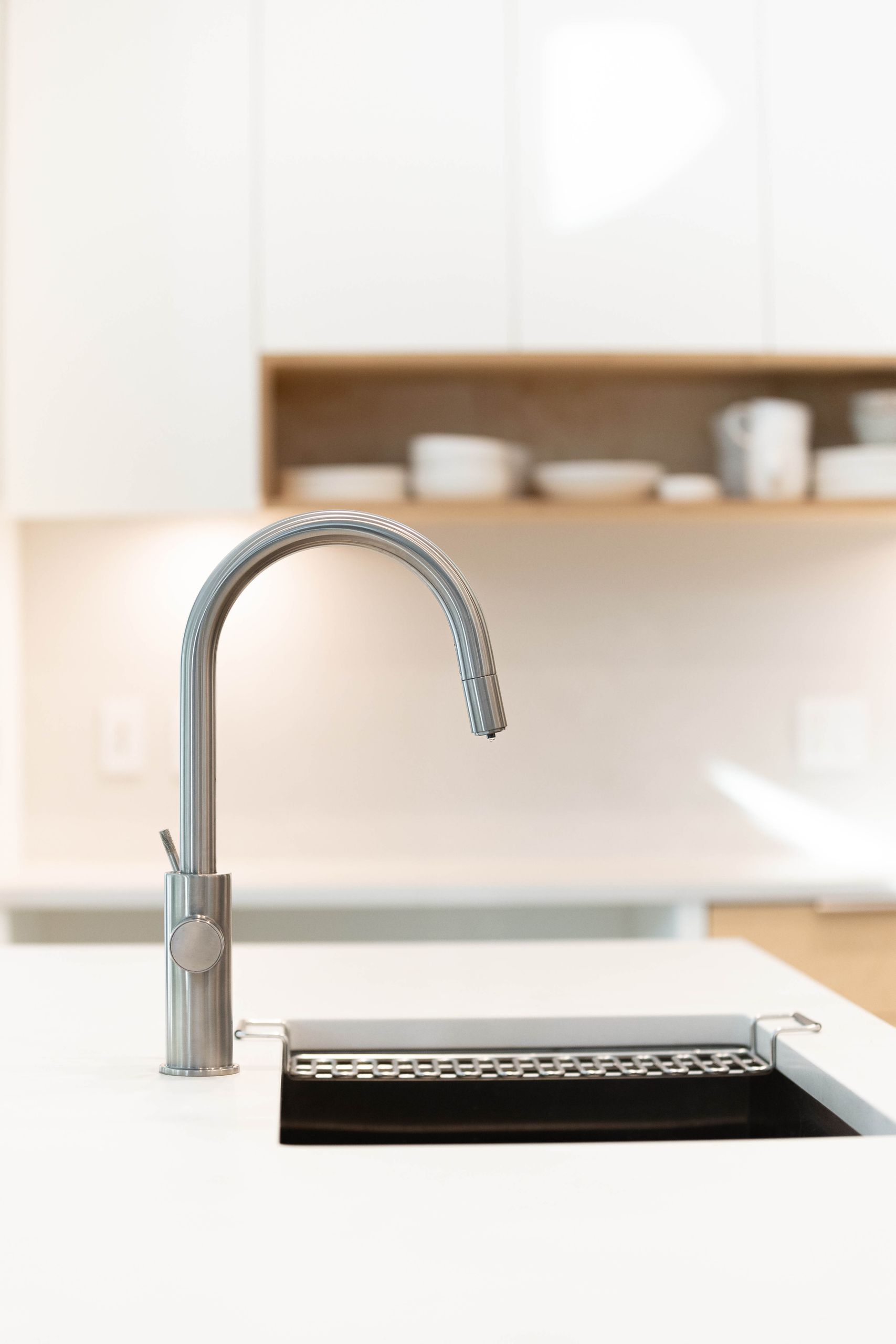 Brushed steel pull-down tap over a black undermount sink in the white island
