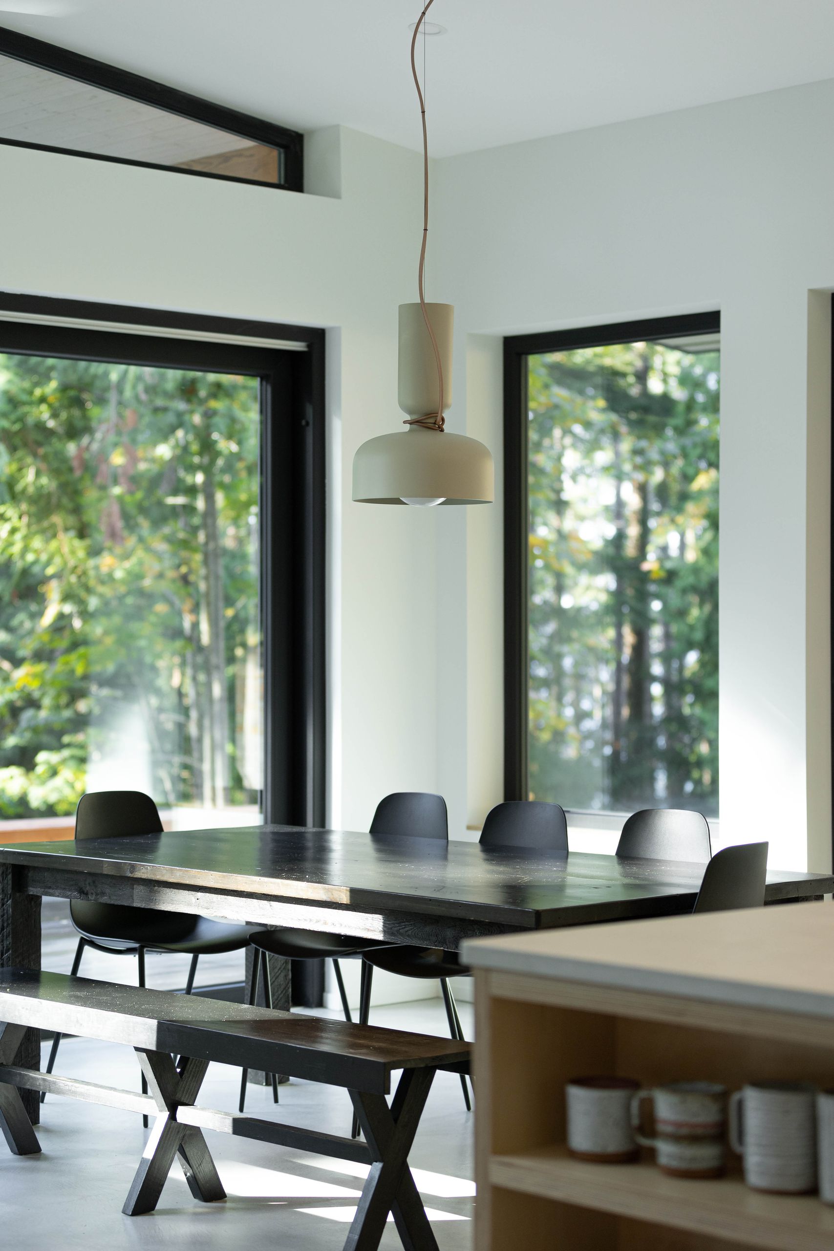 Dining area with a blackened plank table, moulded chairs and a pale dome pendant