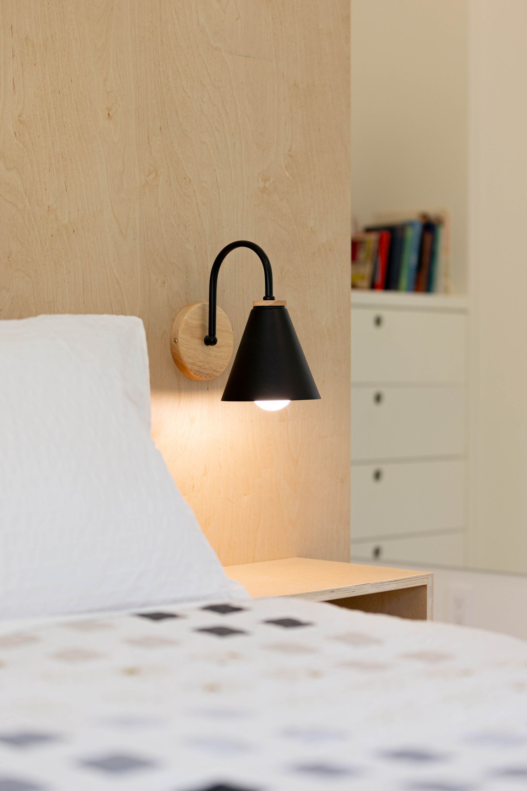 Black cone sconce and floating plywood nightstand against the birch wall