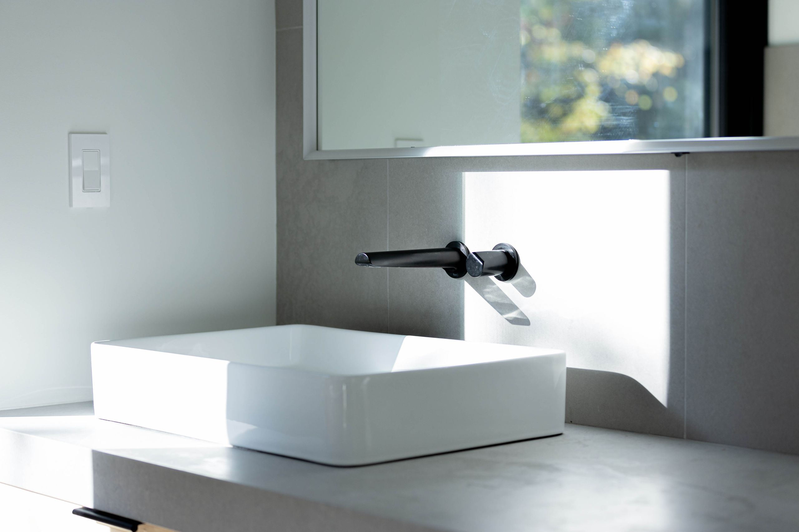 White vessel basin on a concrete counter with a matte black wall-mounted tap