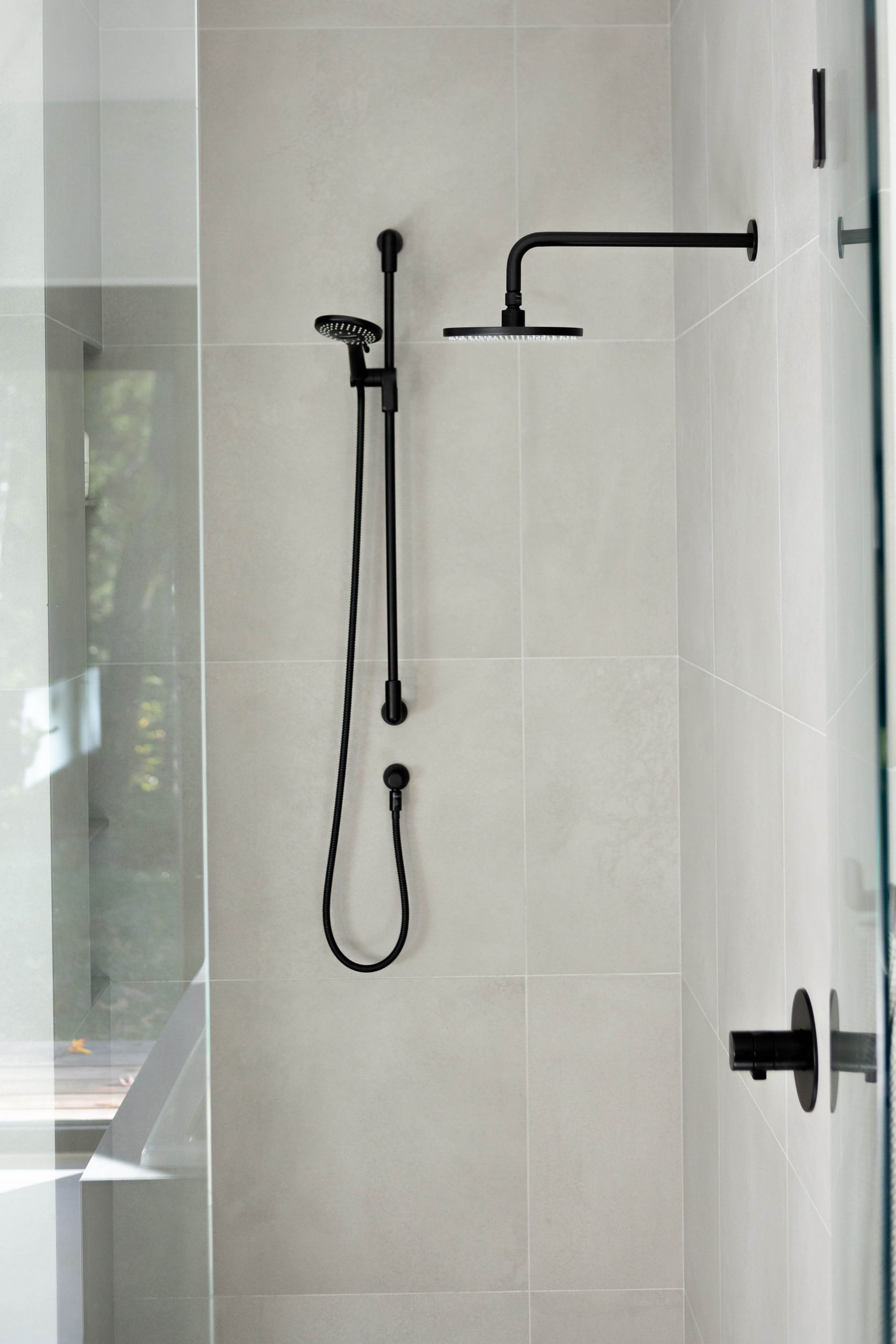Shower with a matte black rain head and slide bar on large-format grey tile