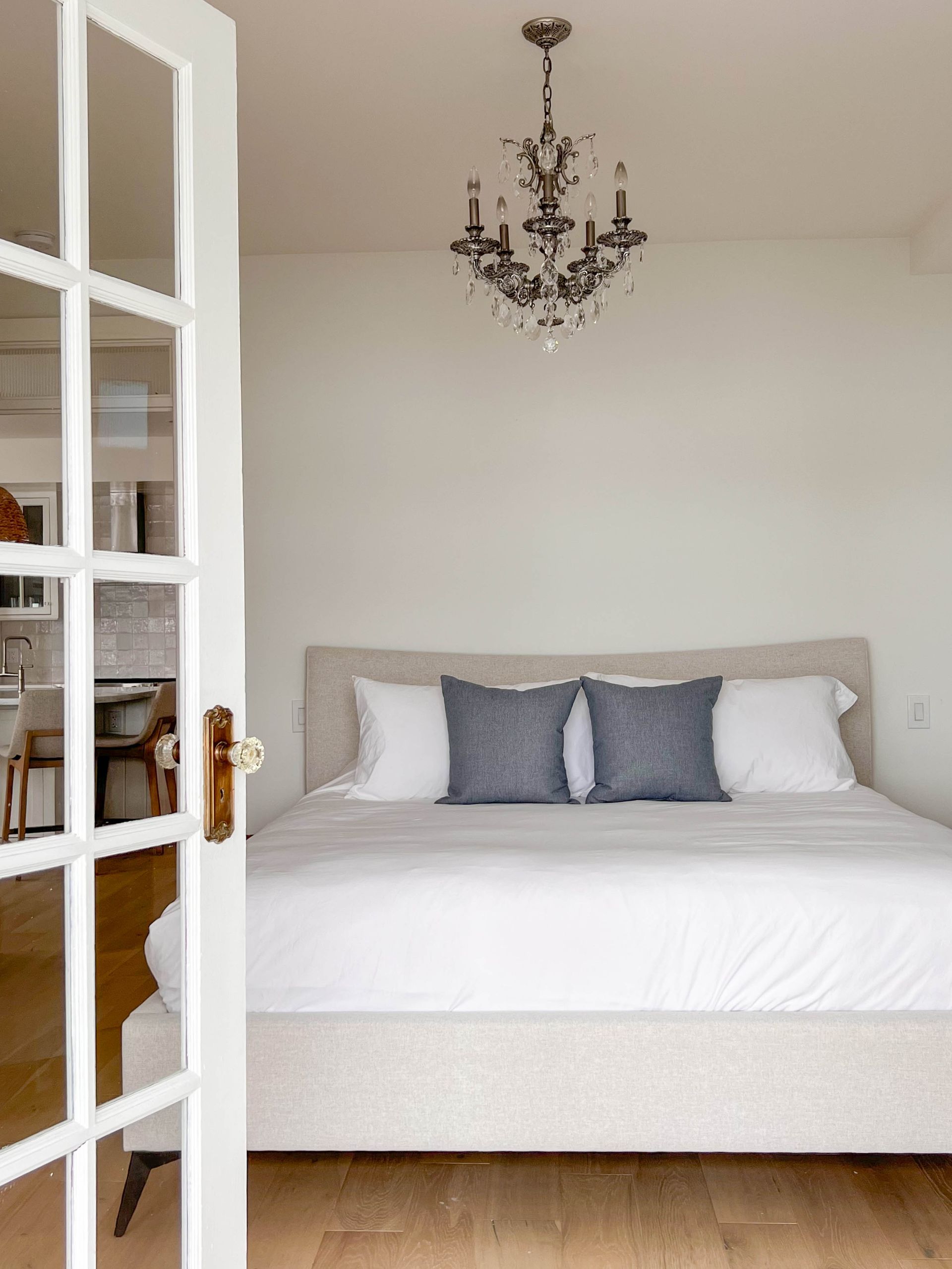 Bedroom seen through a glazed door with a cut-glass knob, a crystal chandelier above the bed