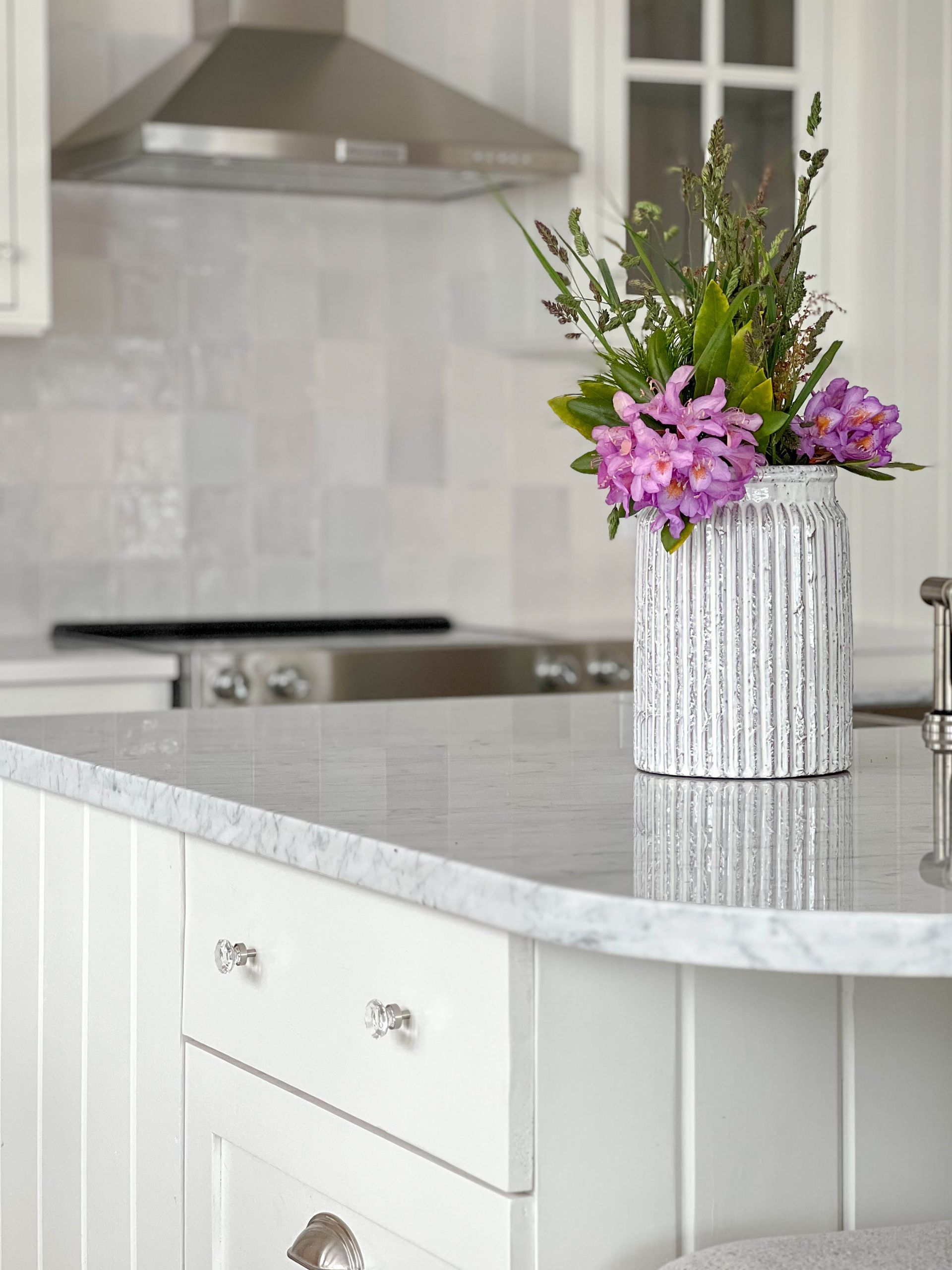 Fluted ceramic vase of rhododendron on the marble island, with zellige tile behind the range
