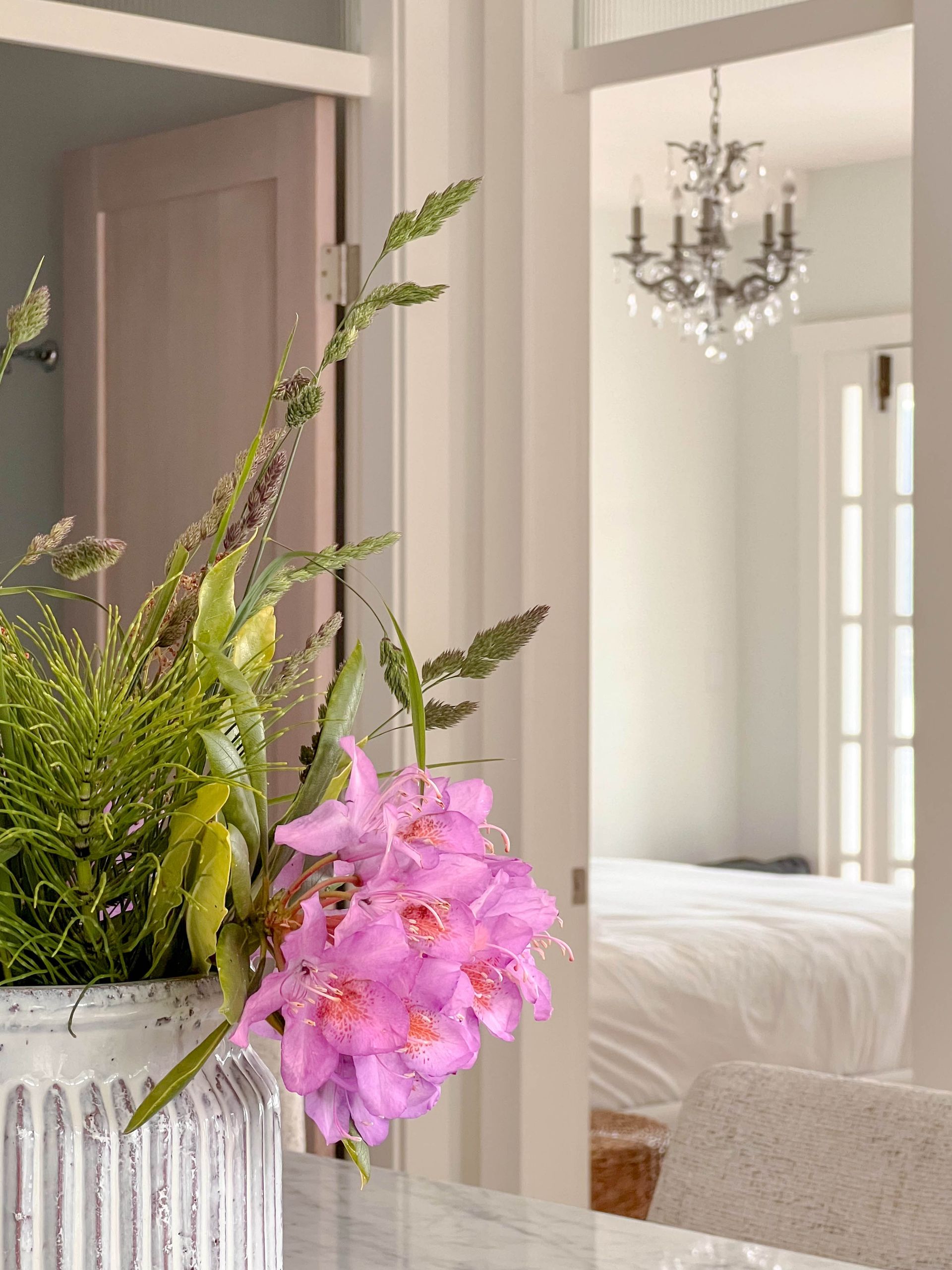 Cut rhododendron and grasses on the counter, looking through to the bedroom beyond