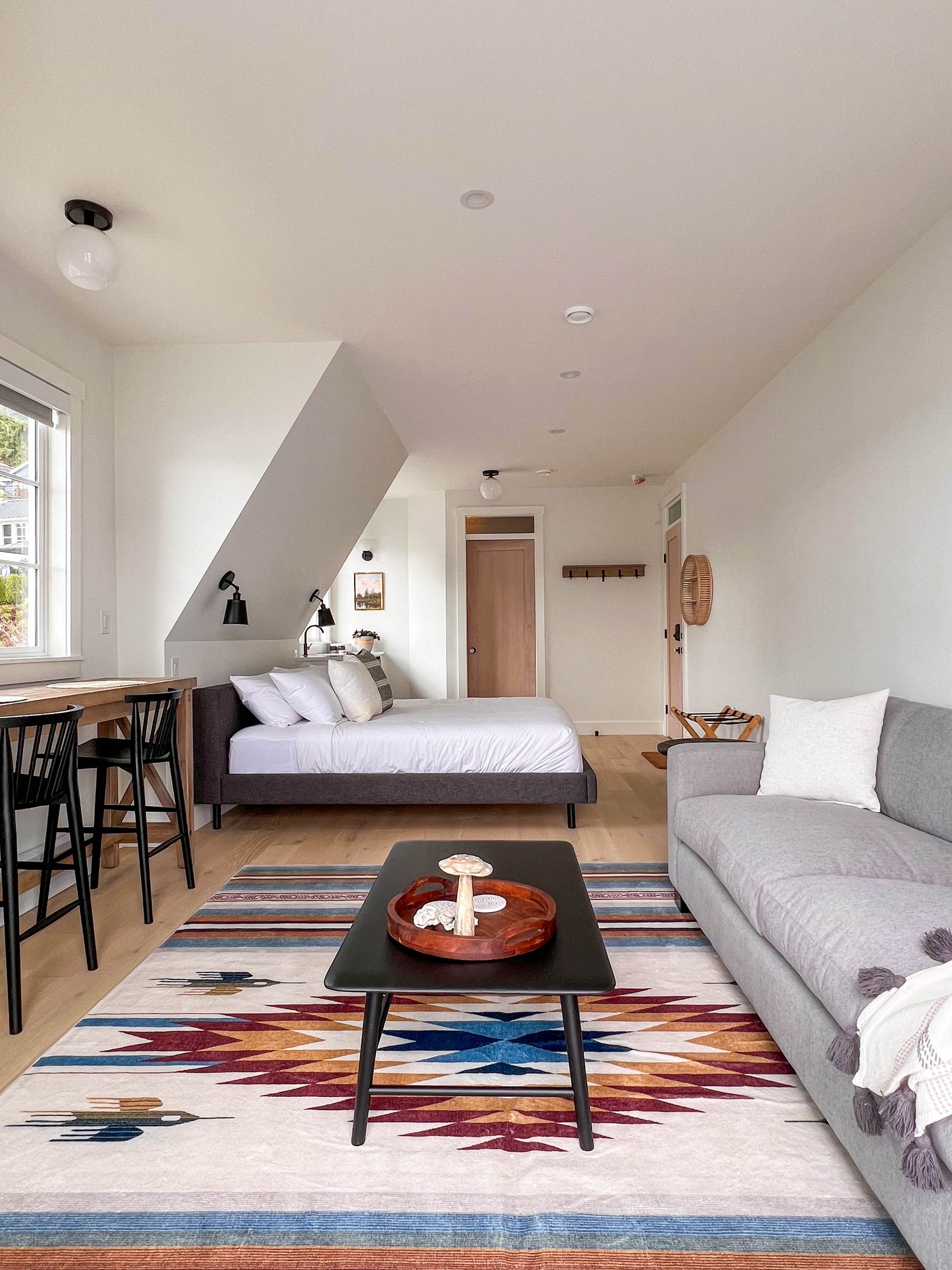 Studio suite with a bed, sofa and patterned wool rug beneath the sloped dormer ceiling