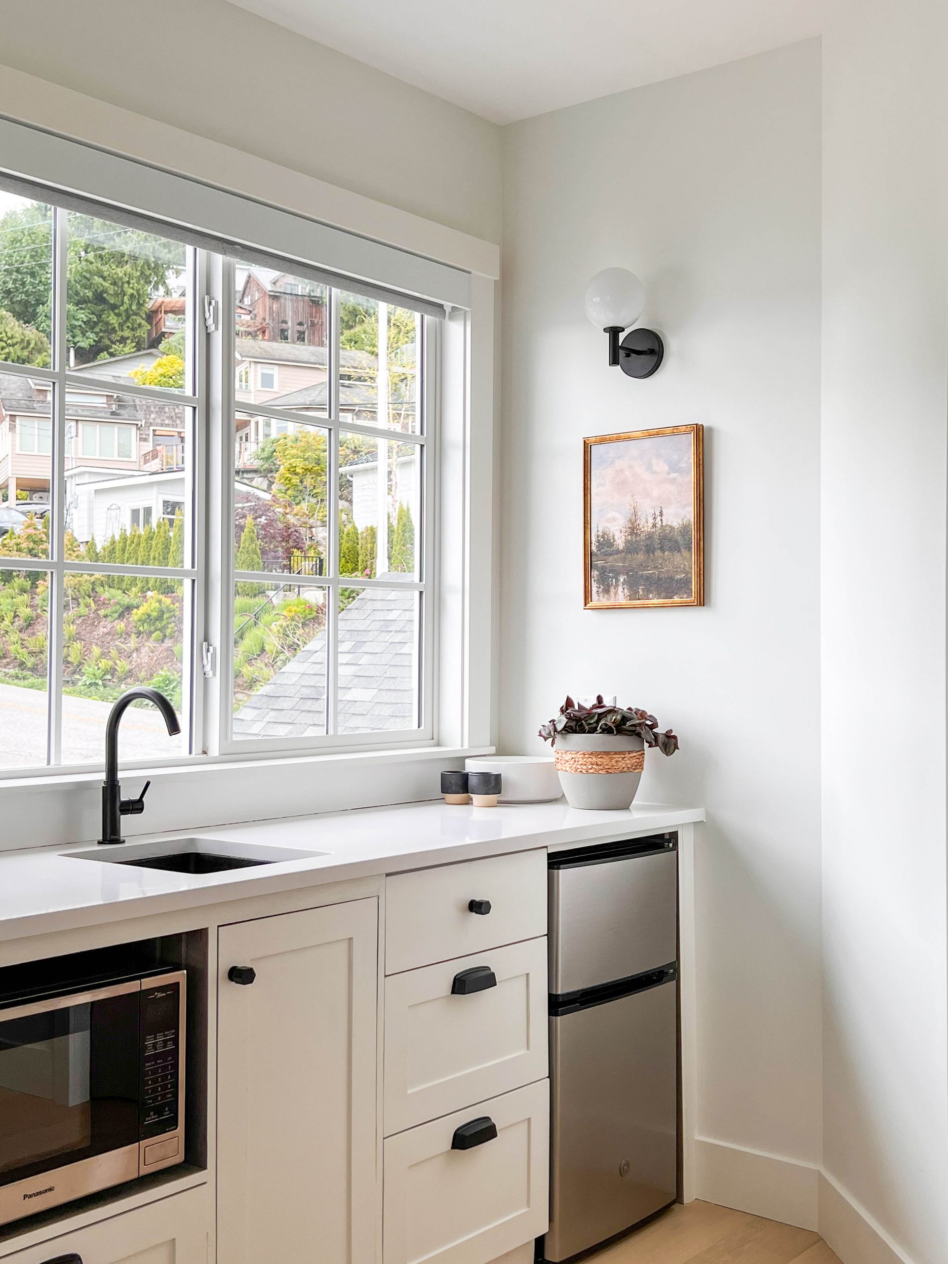Kitchenette with a black faucet, bar fridge and a gilt-framed landscape painting