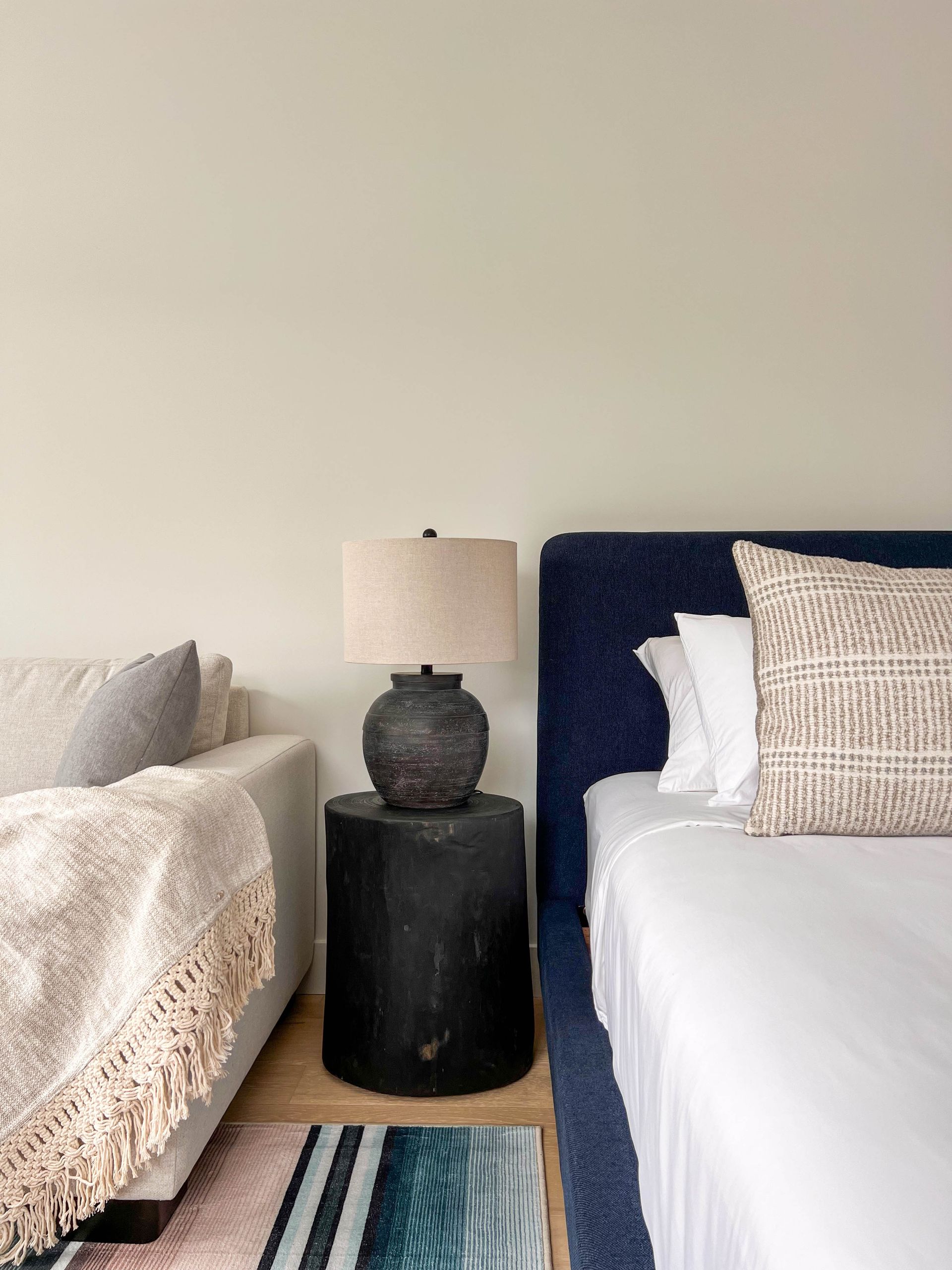 Black urn lamp on a round wood side table between the sofa and the navy bed