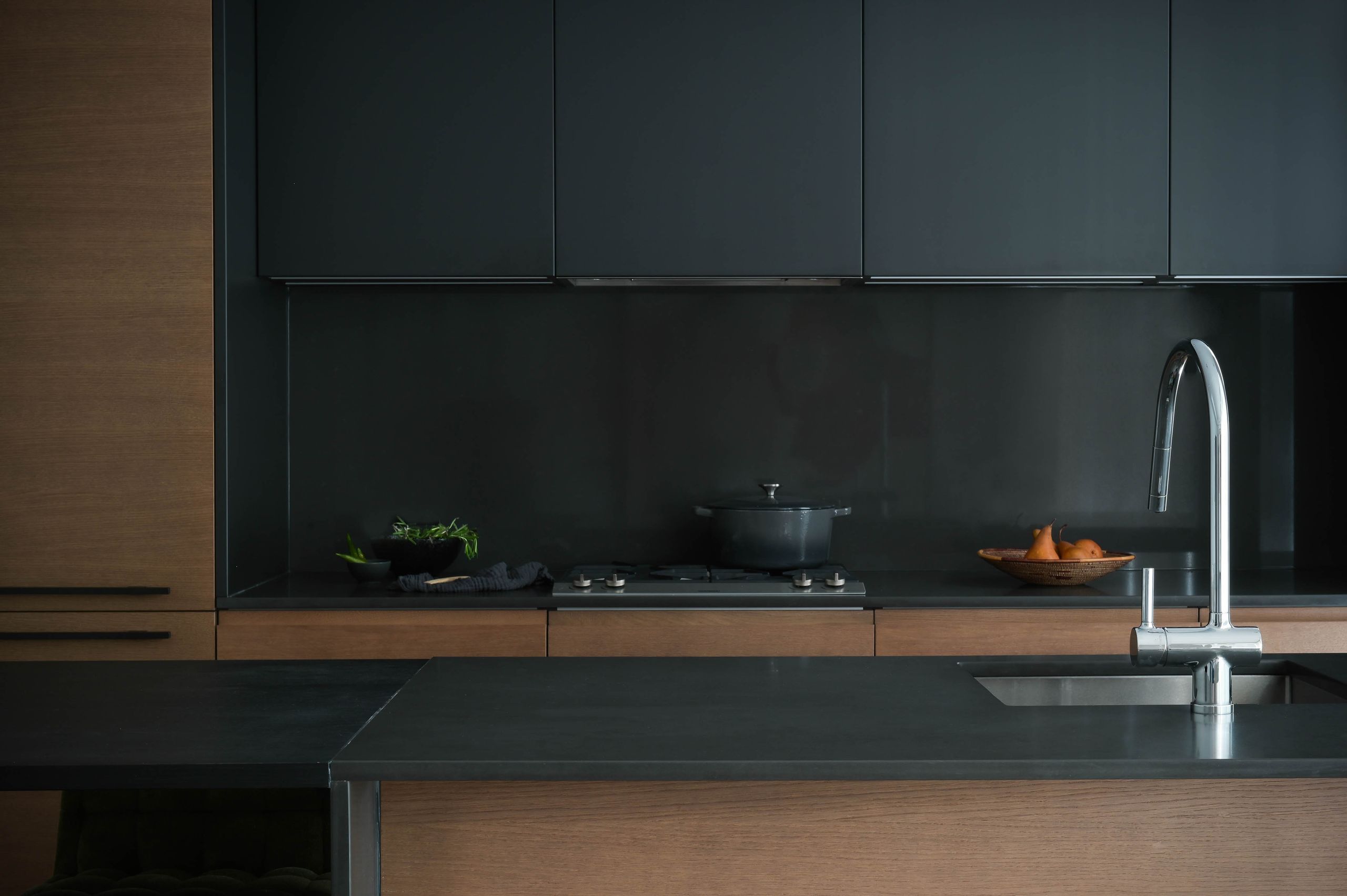 Kitchen with matte black uppers, a black glass backsplash and oak lower cabinets