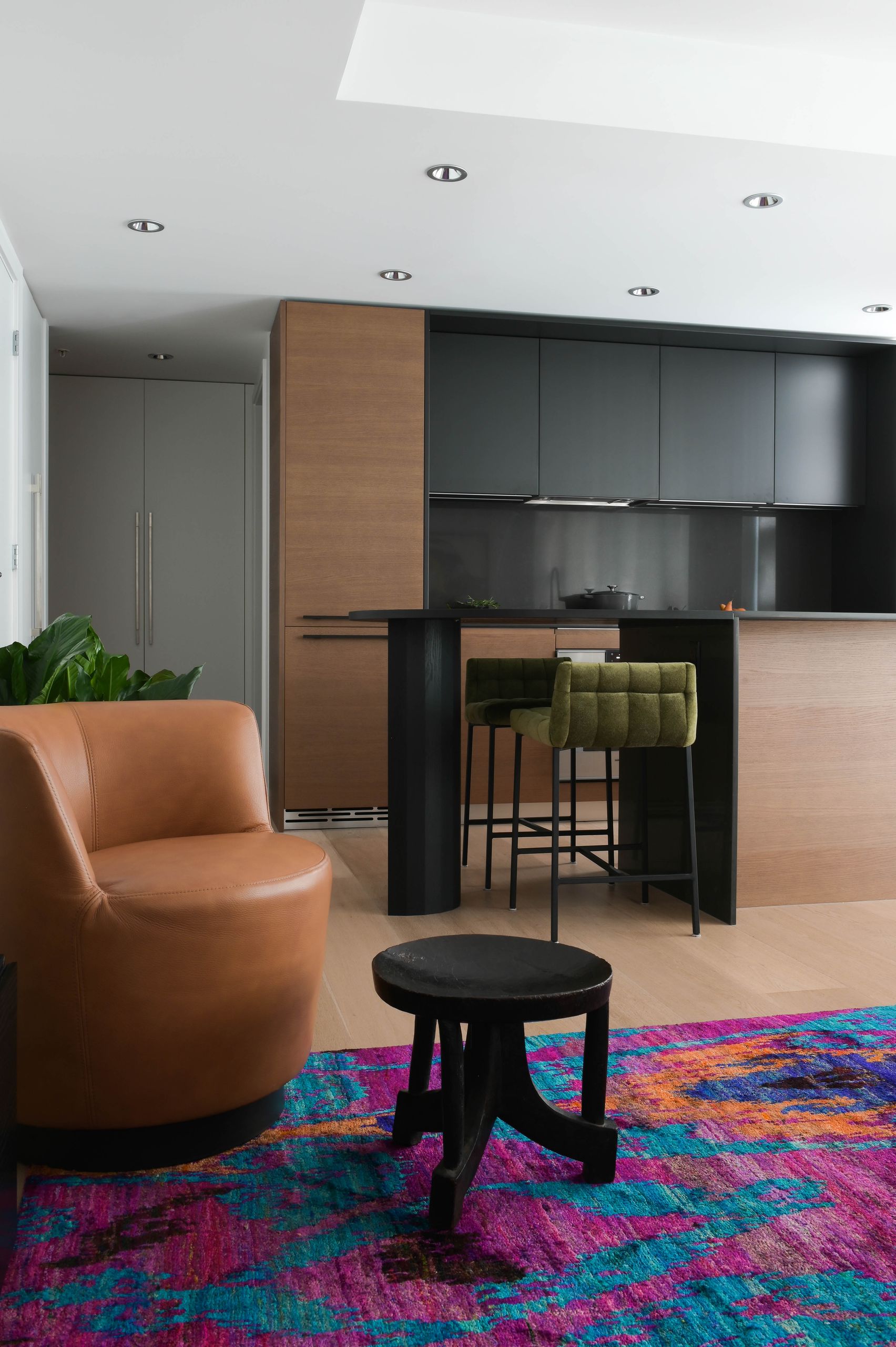 Tan leather swivel chair and carved stool on the magenta silk rug, facing the galley kitchen