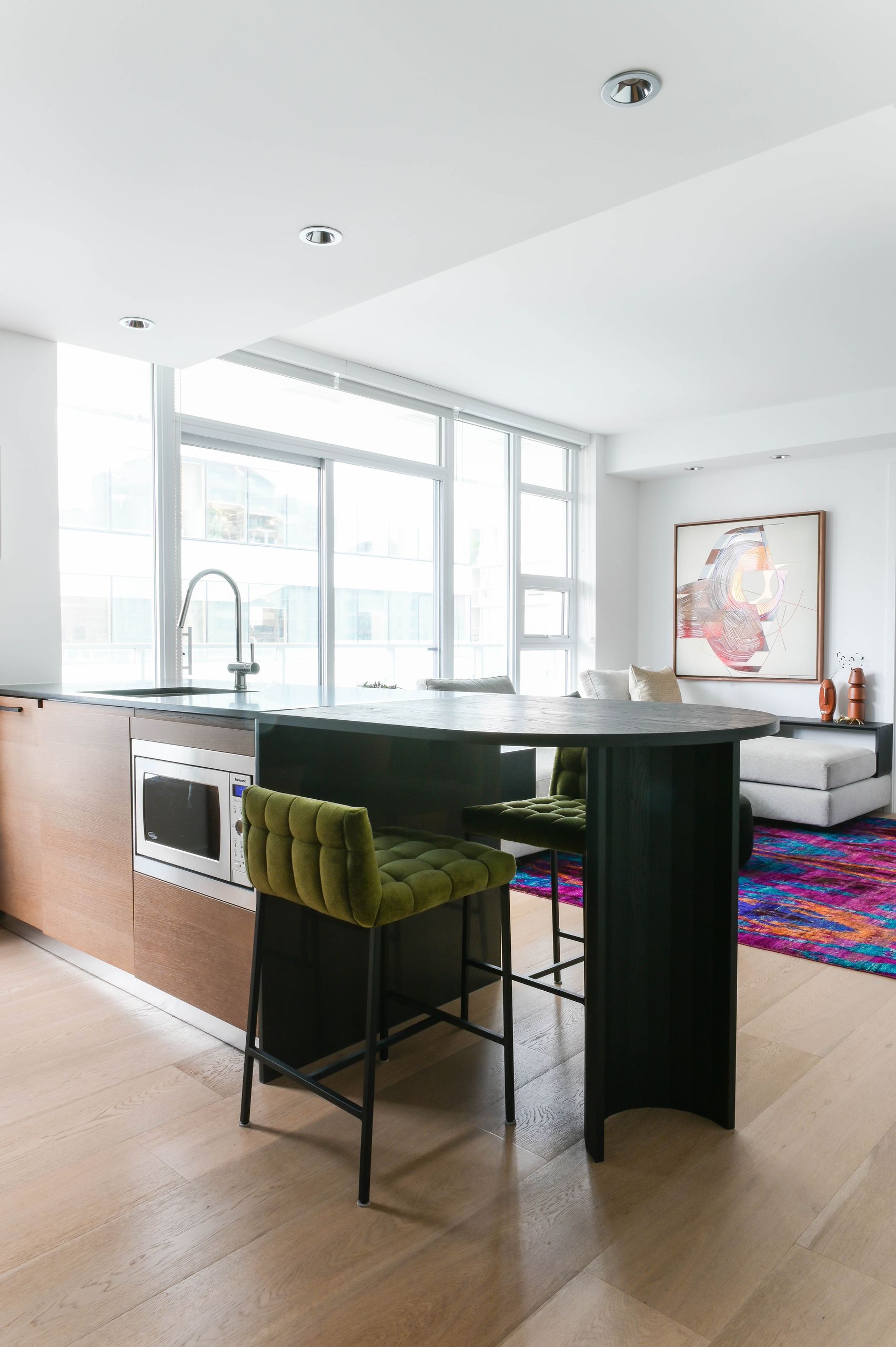 Black curved peninsula with green velvet stools, looking through to the living room