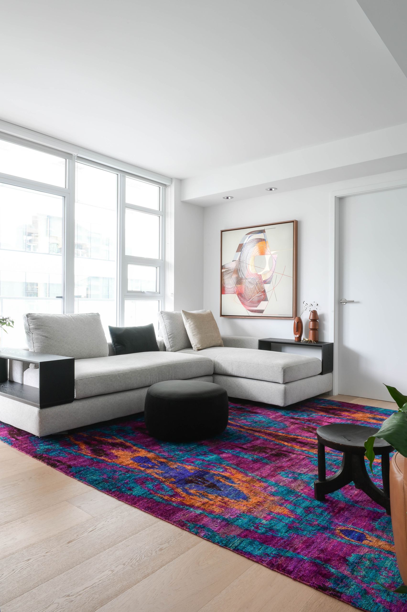 Living room with a grey sectional, black pouf and the silk rug in magenta and teal