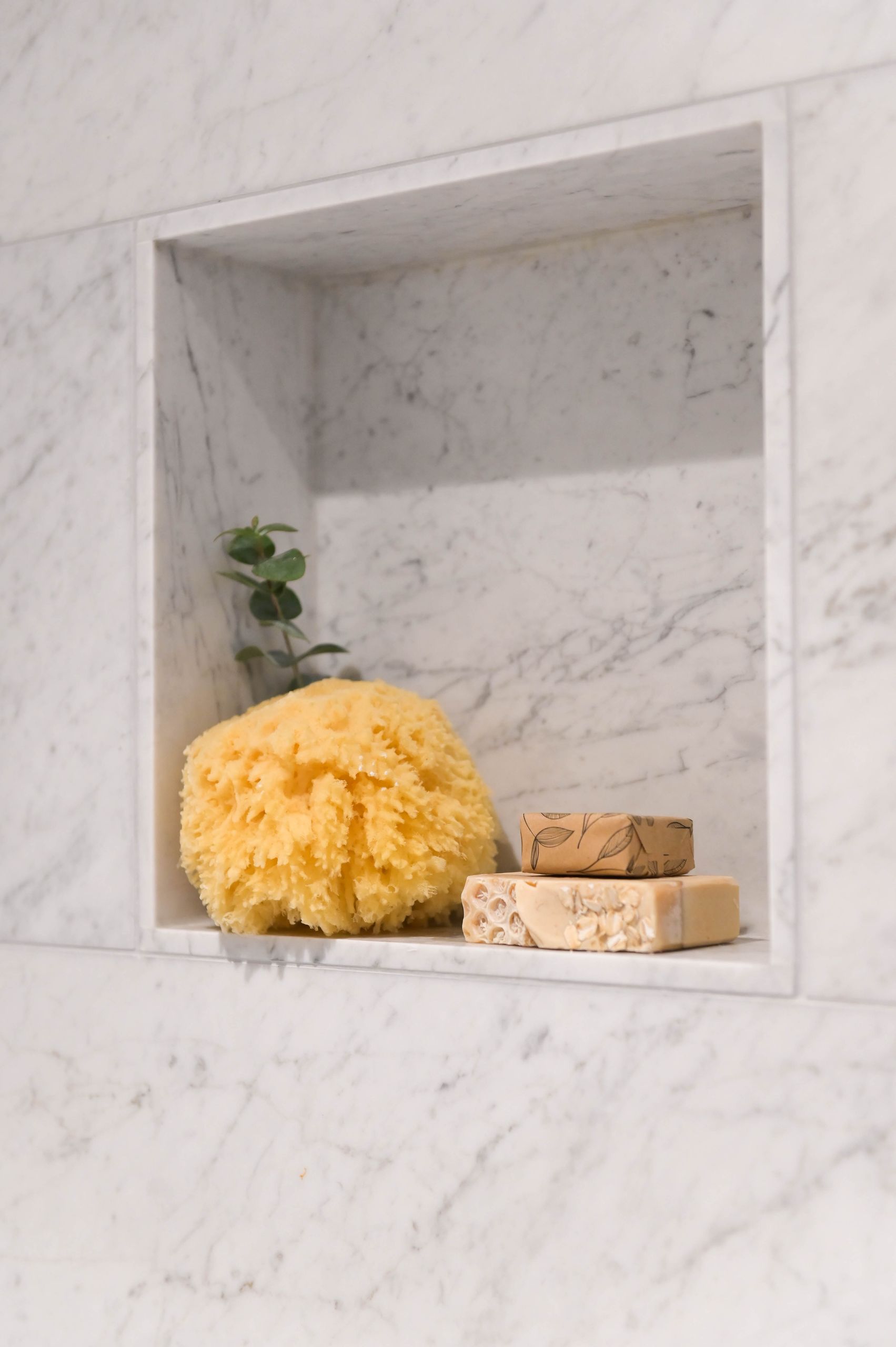 Marble shower niche holding a sea sponge, soap bars and a sprig of eucalyptus