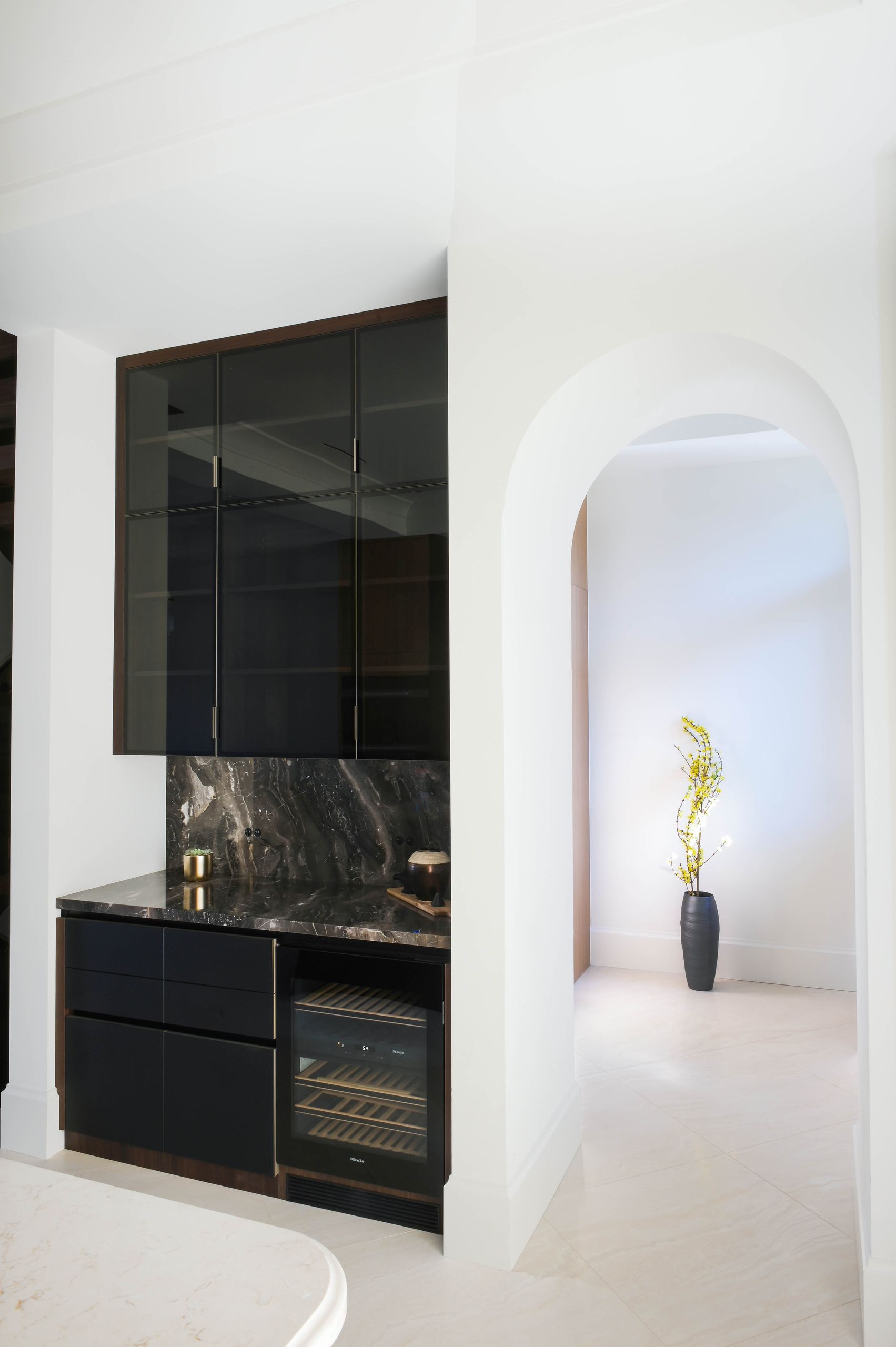 Servery with smoked glass cabinets, marble counter and an arched opening beyond