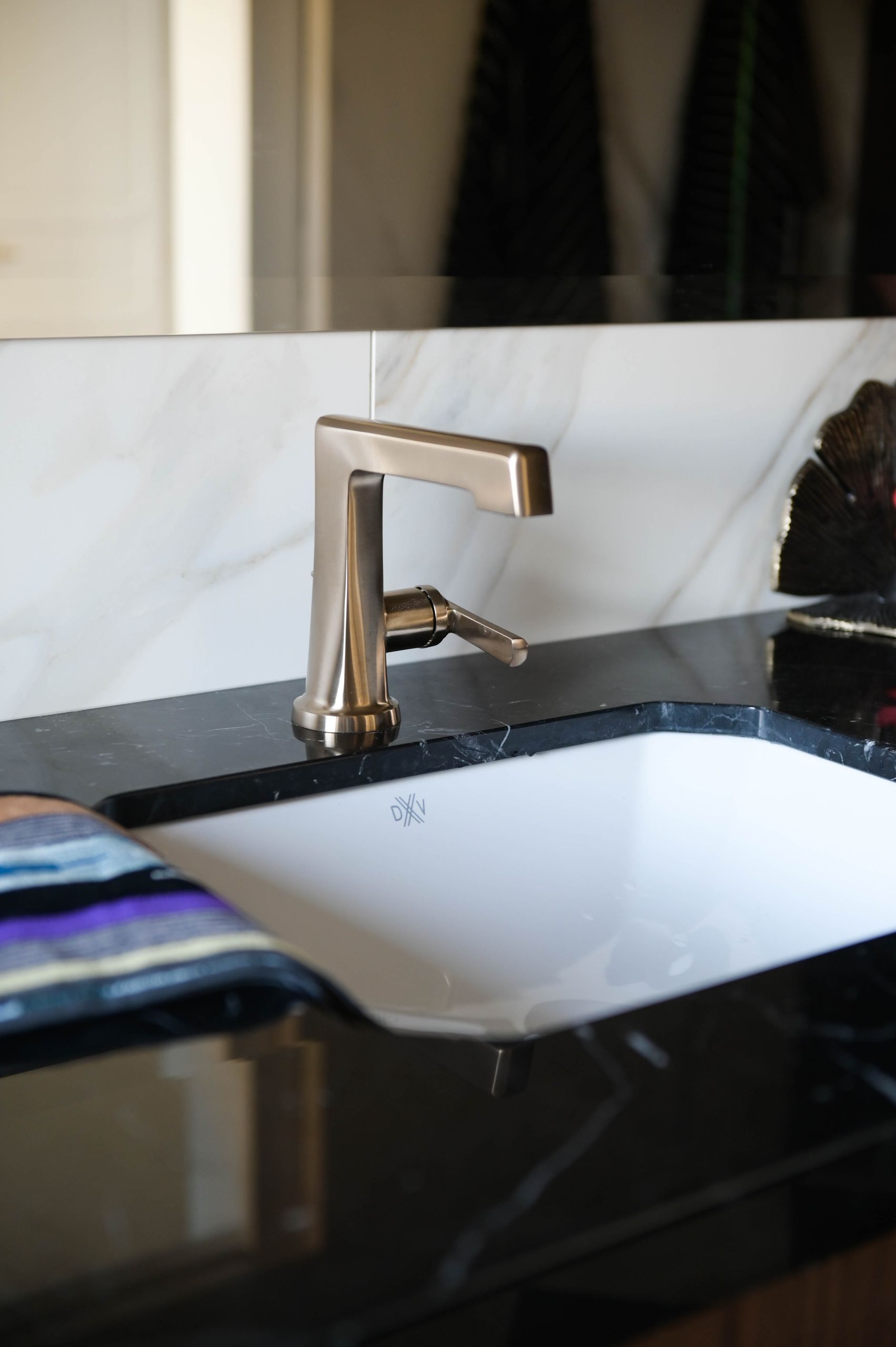 Brushed brass basin tap on the black marble counter against calacatta marble