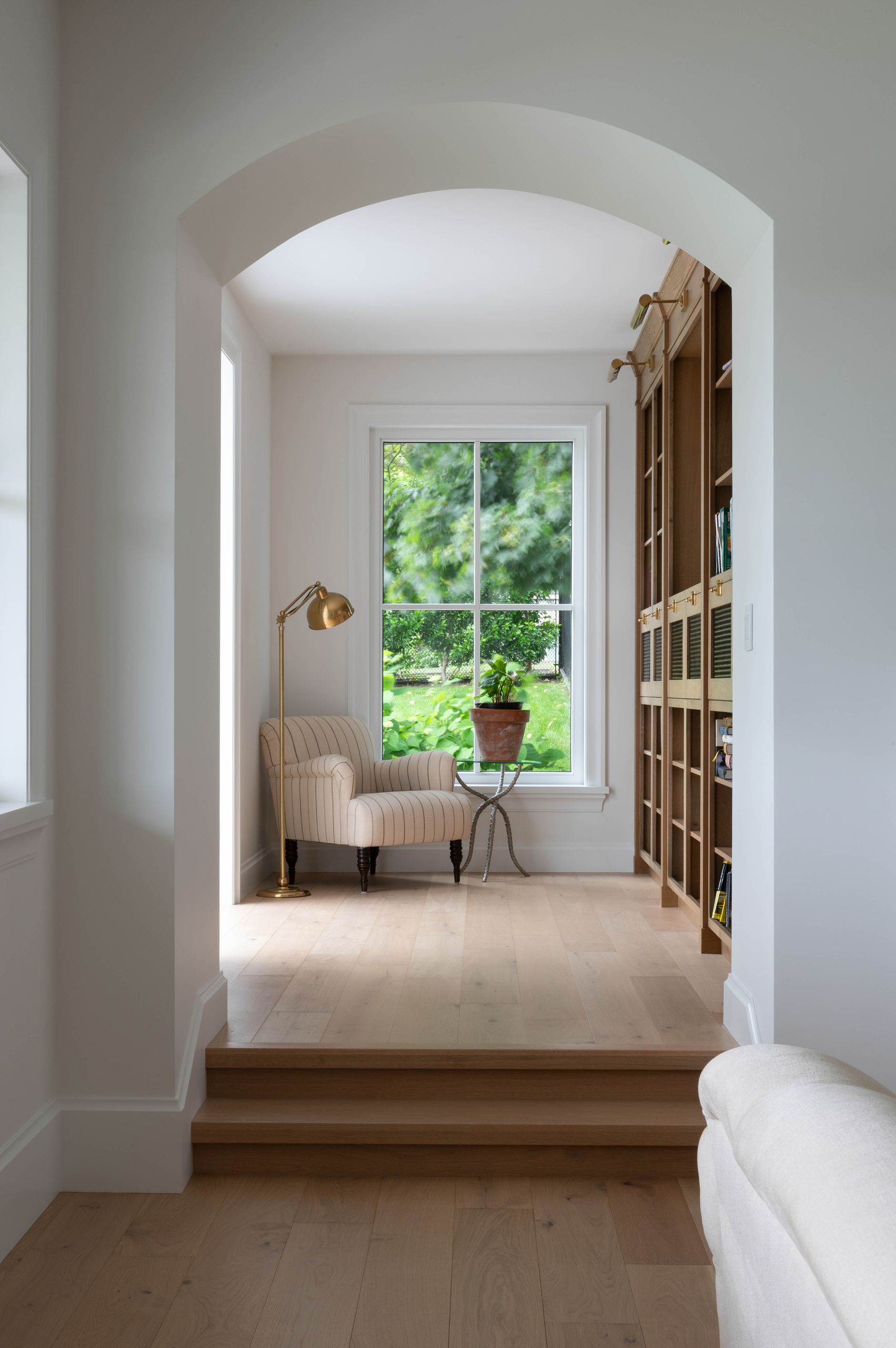 Arched opening onto a raised reading nook with a striped armchair and built-in oak bookshelves