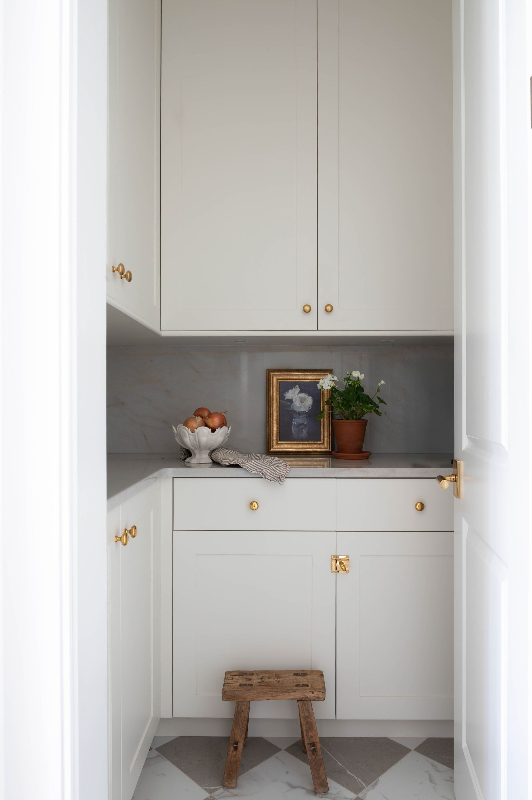 Walk-in pantry with brass latches, marble counters and a checkerboard marble floor