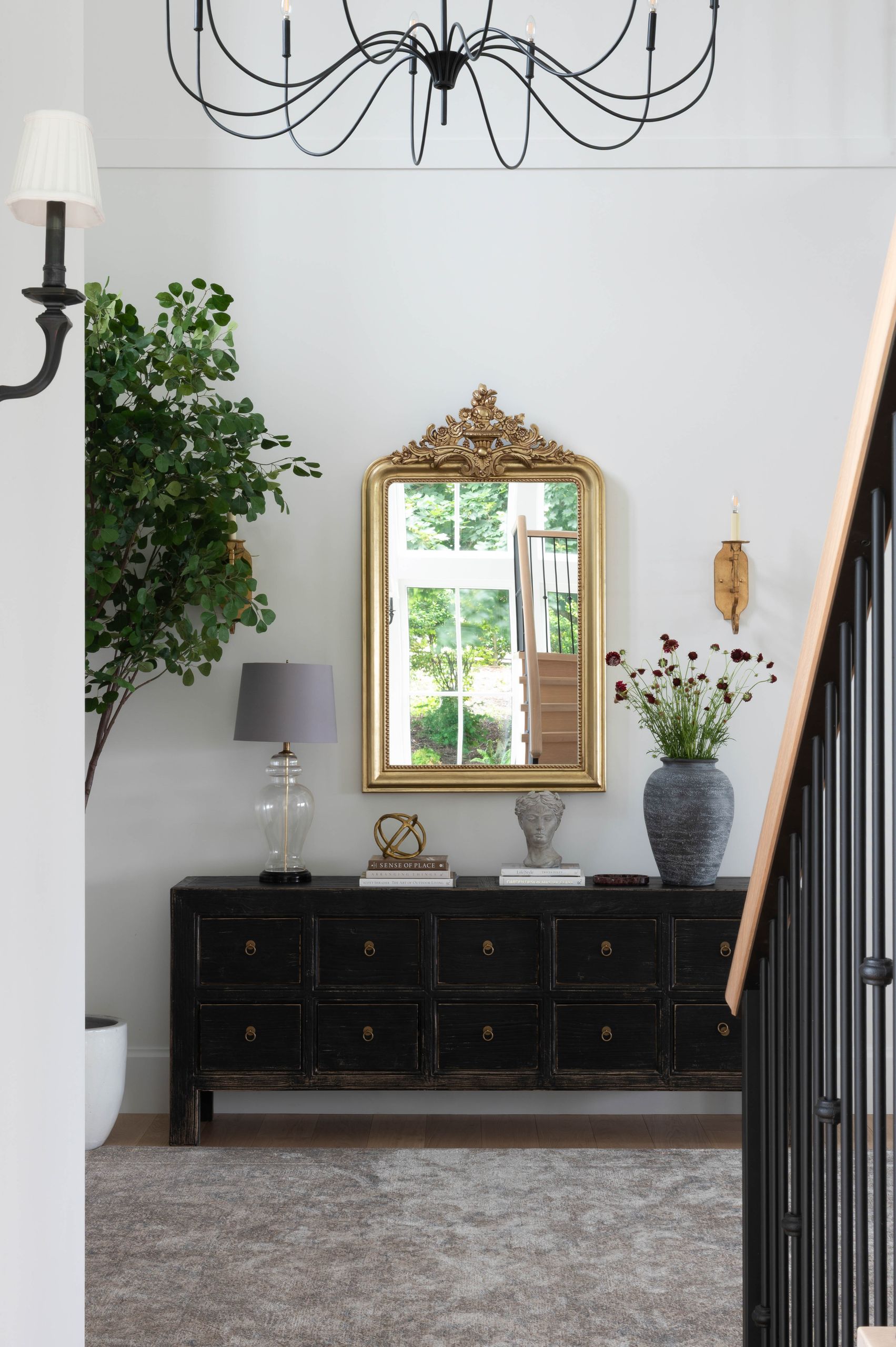 Entry hall with a black apothecary console, gilt mirror and wrought-iron chandelier beside the stair