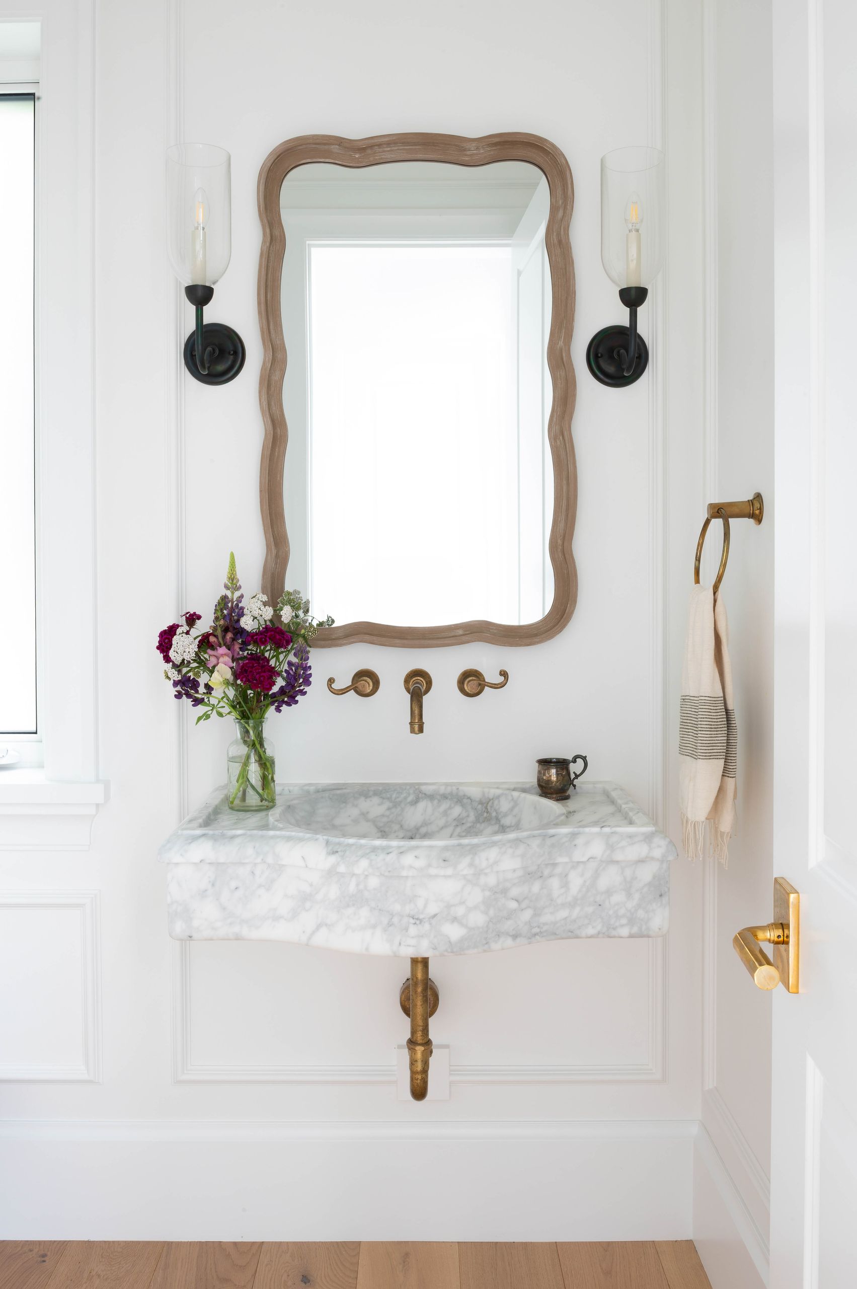 Powder room with a carved wavy-edged mirror above a solid marble wall-mounted basin