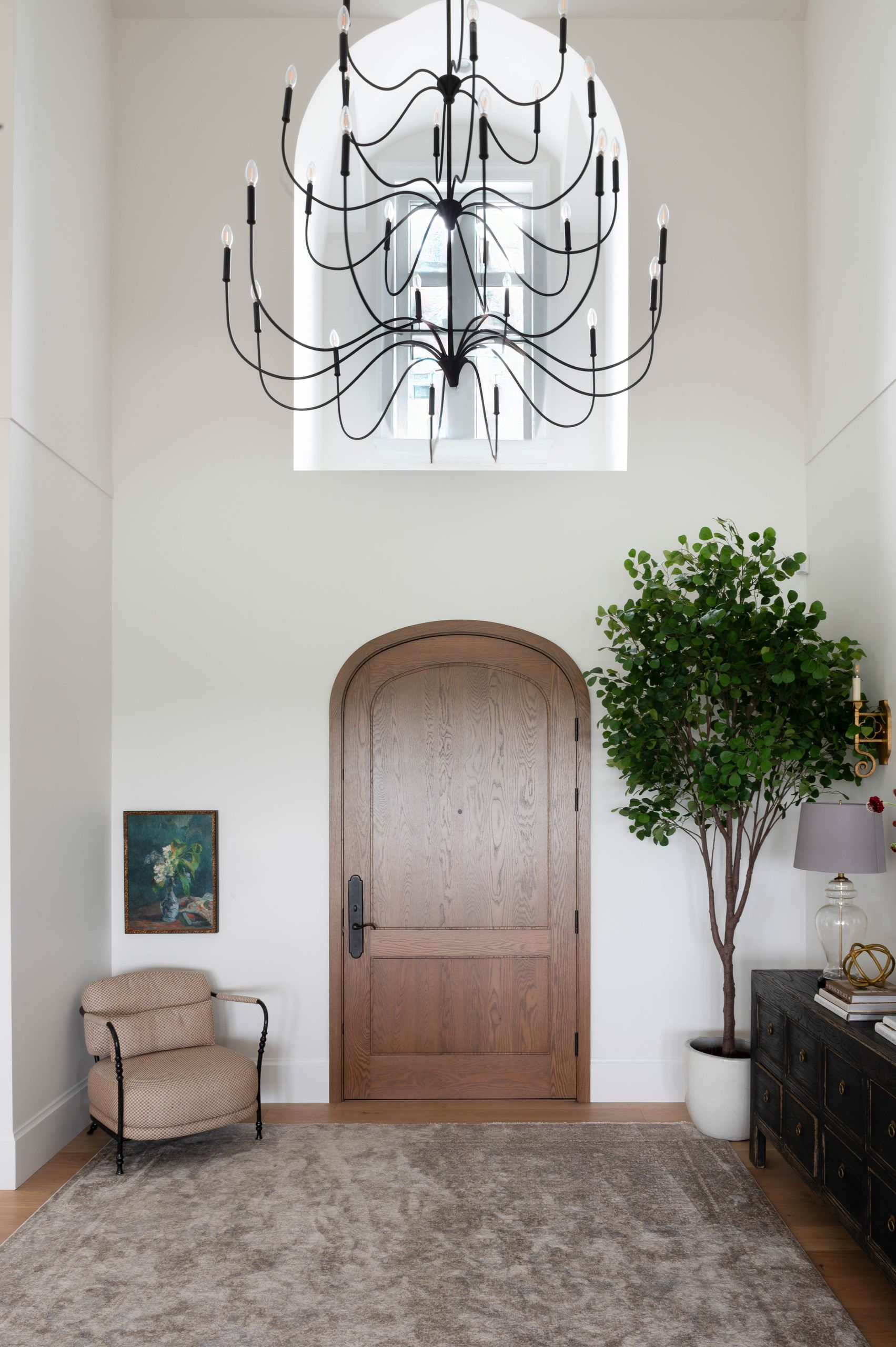 Double-height entry with an arched white-oak front door and a black iron chandelier
