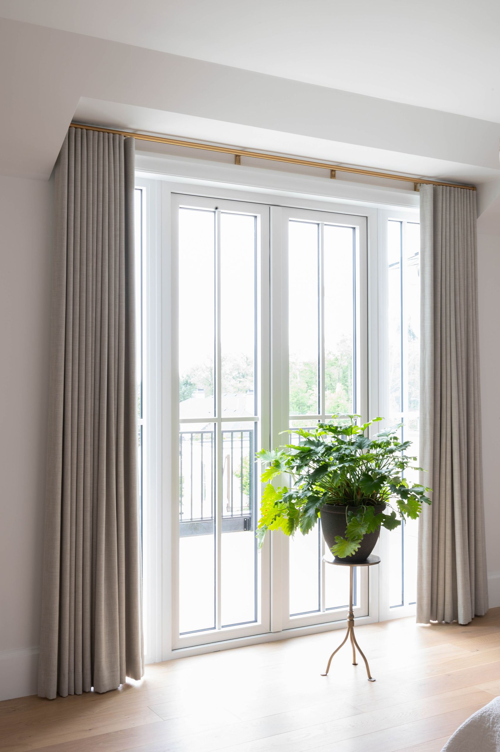 Bedroom French doors onto a balcony, framed by linen drapery on a brass rod