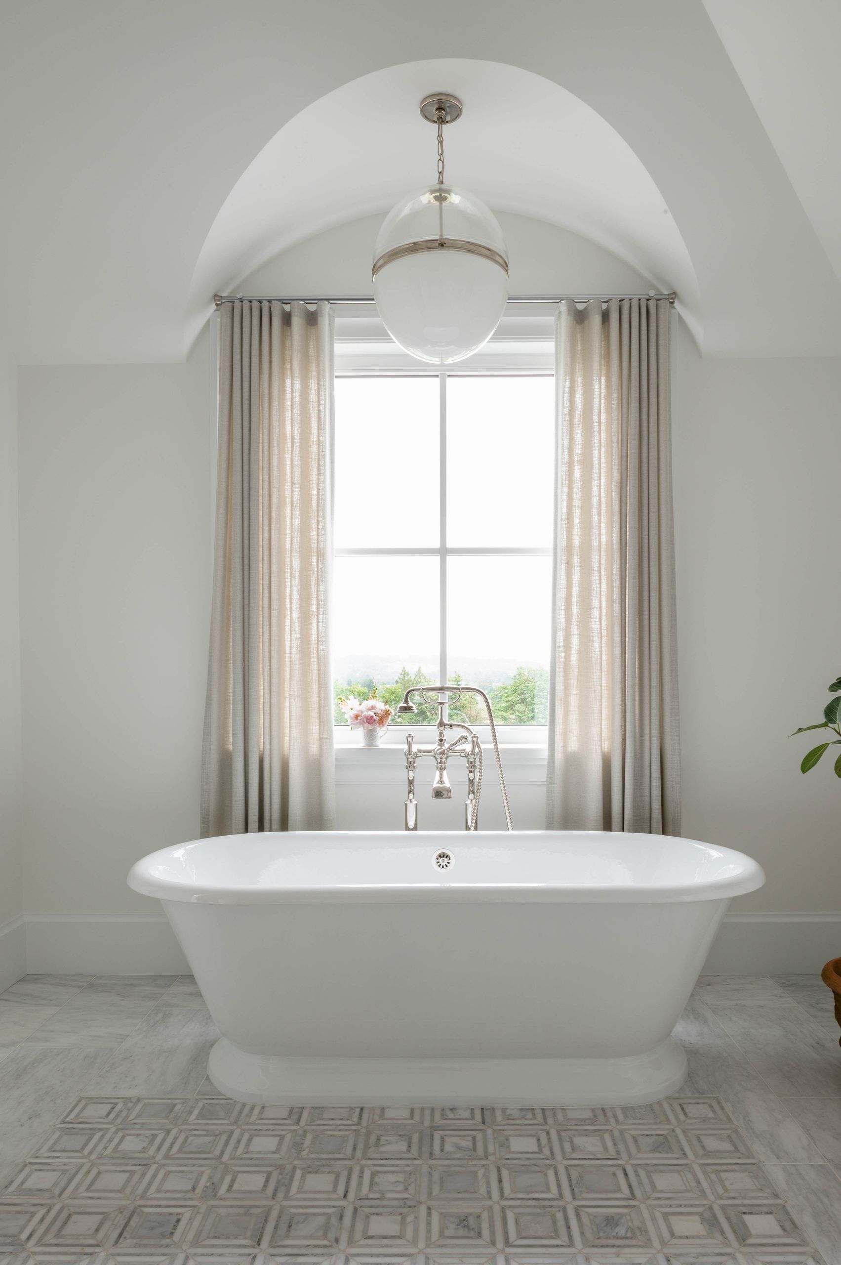 Freestanding roll-top tub set into a barrel-vaulted alcove beneath a glass globe pendant