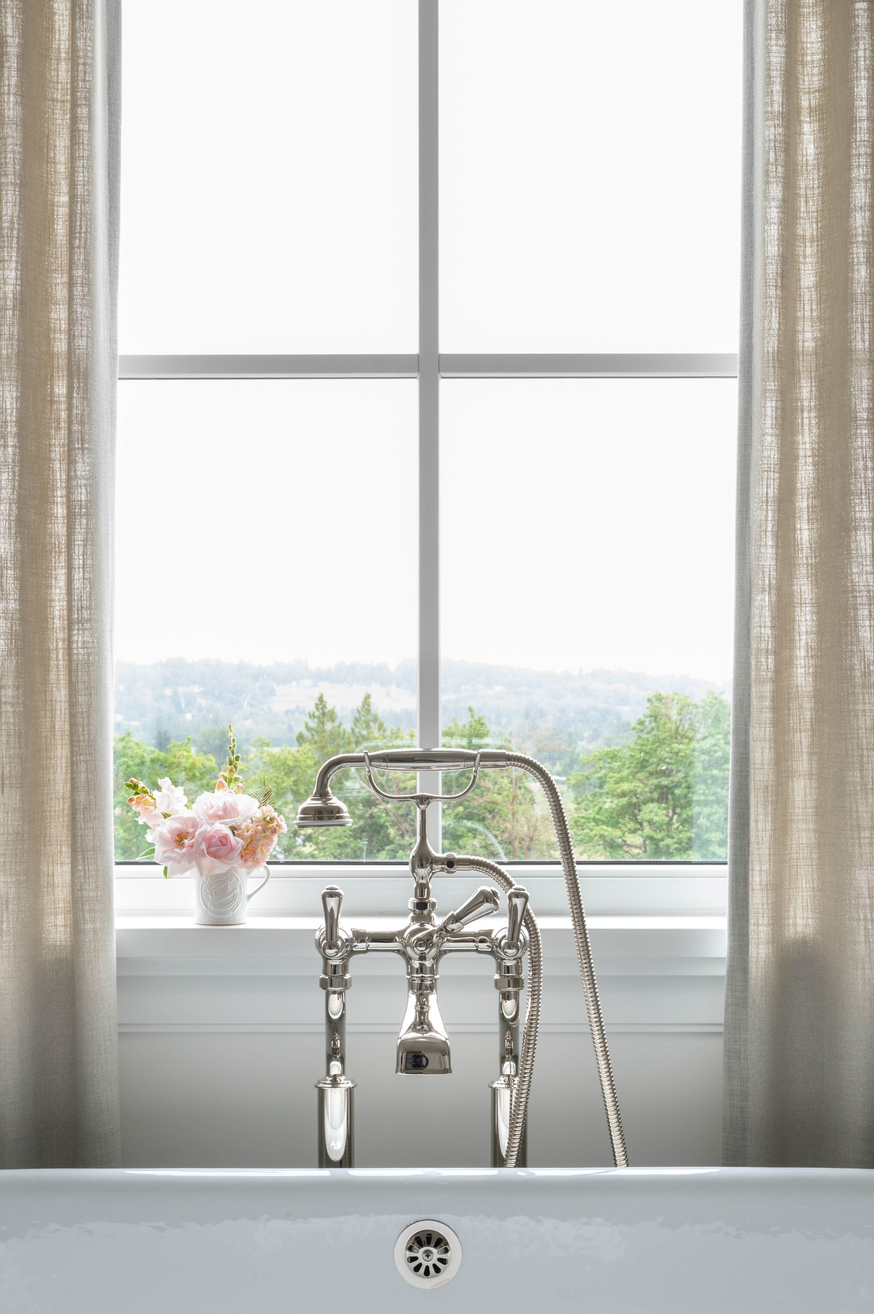 Polished nickel tub filler with a jug of roses on the sill above the valley view