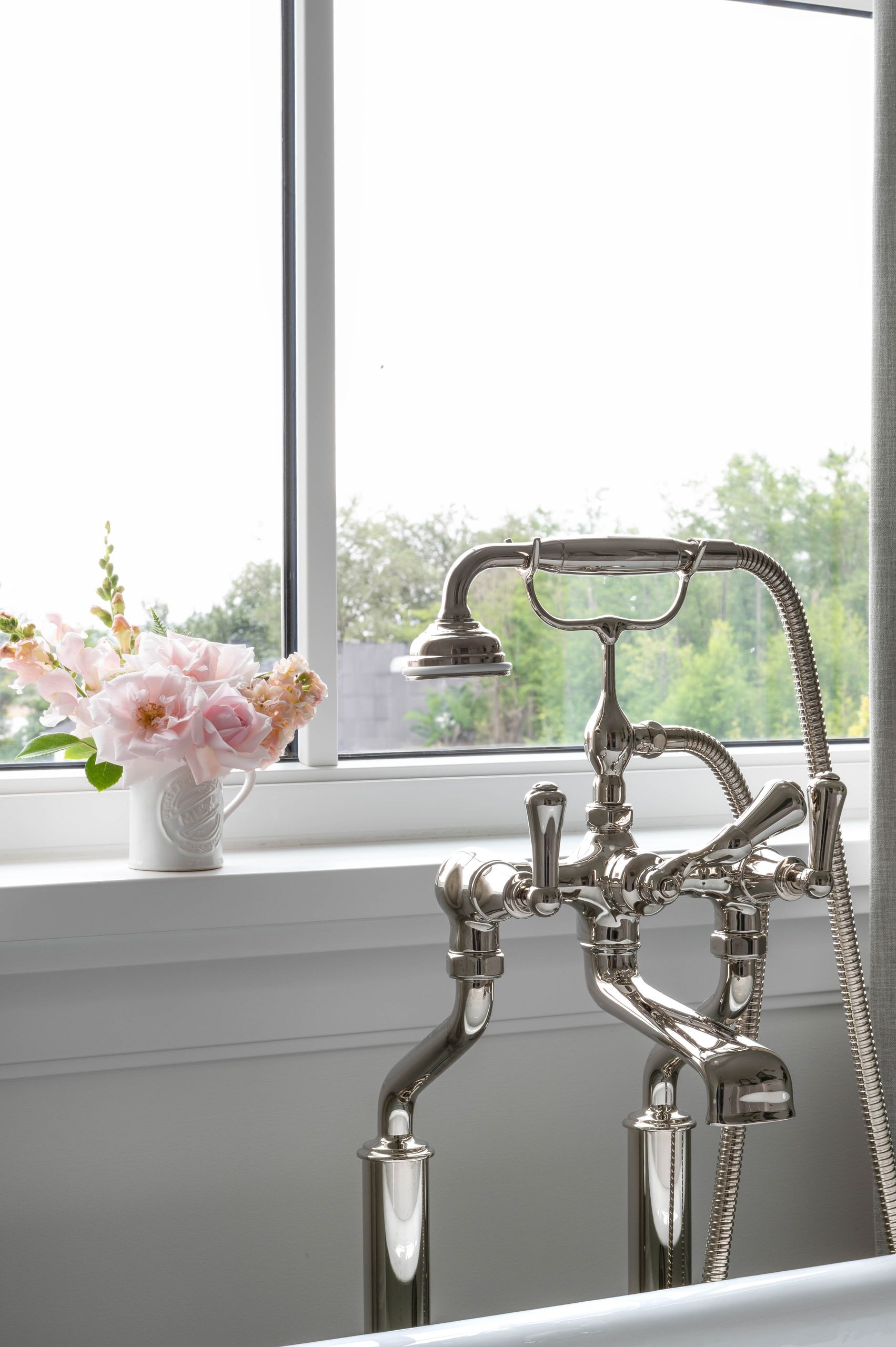 Detail of the telephone-style tub filler beside garden roses in a ceramic jug