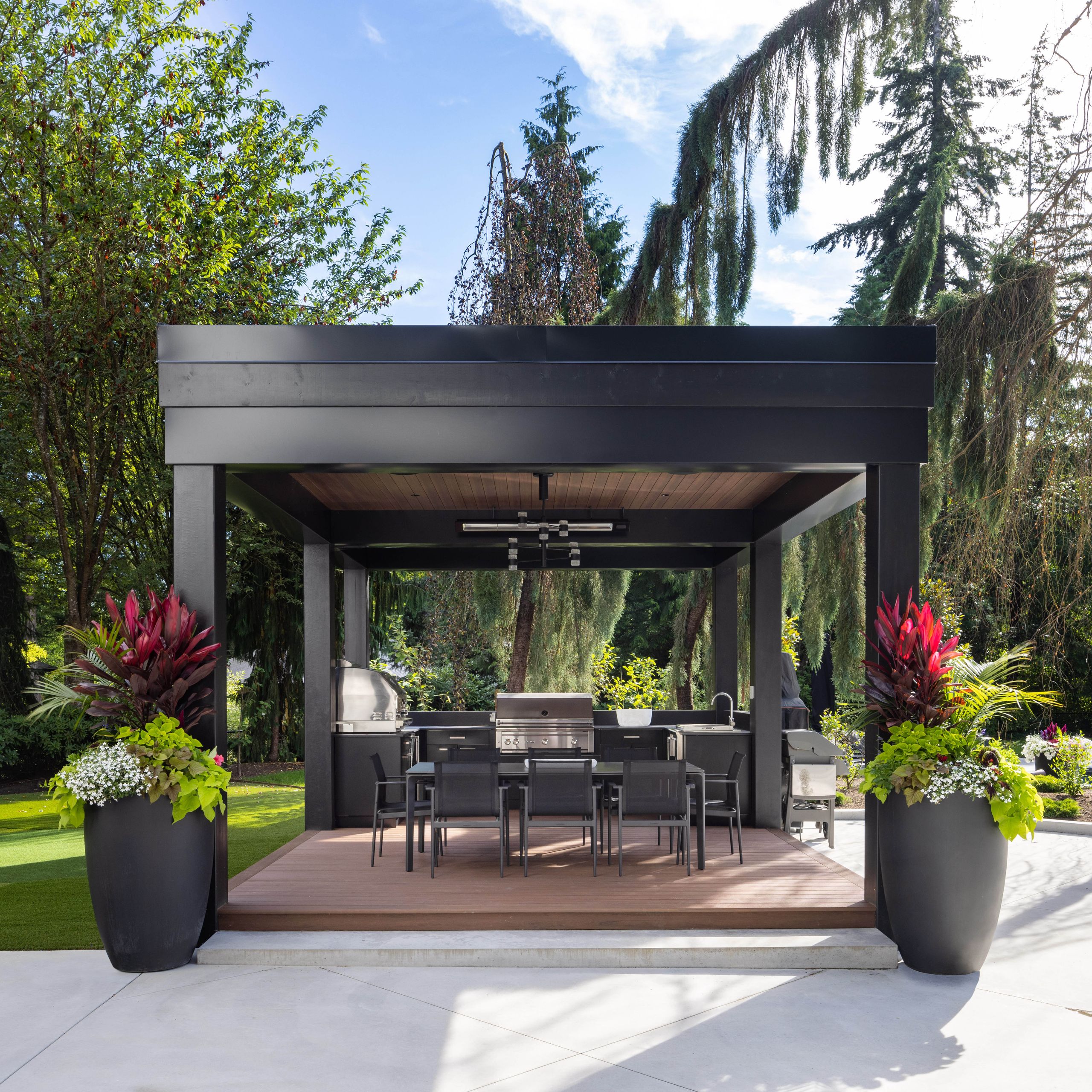 Black steel outdoor kitchen pavilion with a cedar ceiling, grill and dining table