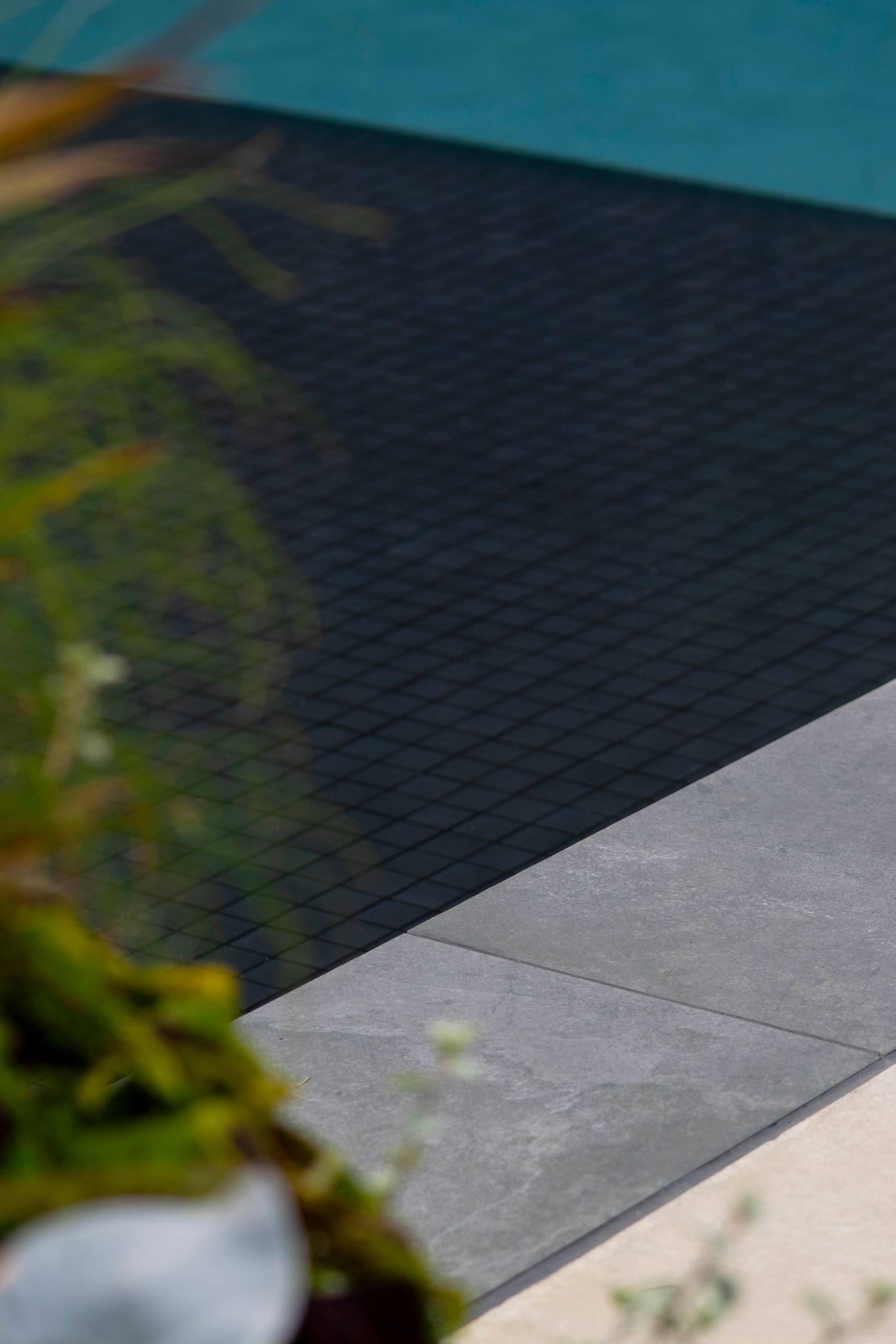 Detail of the black mosaic pool tile meeting the grey stone coping
