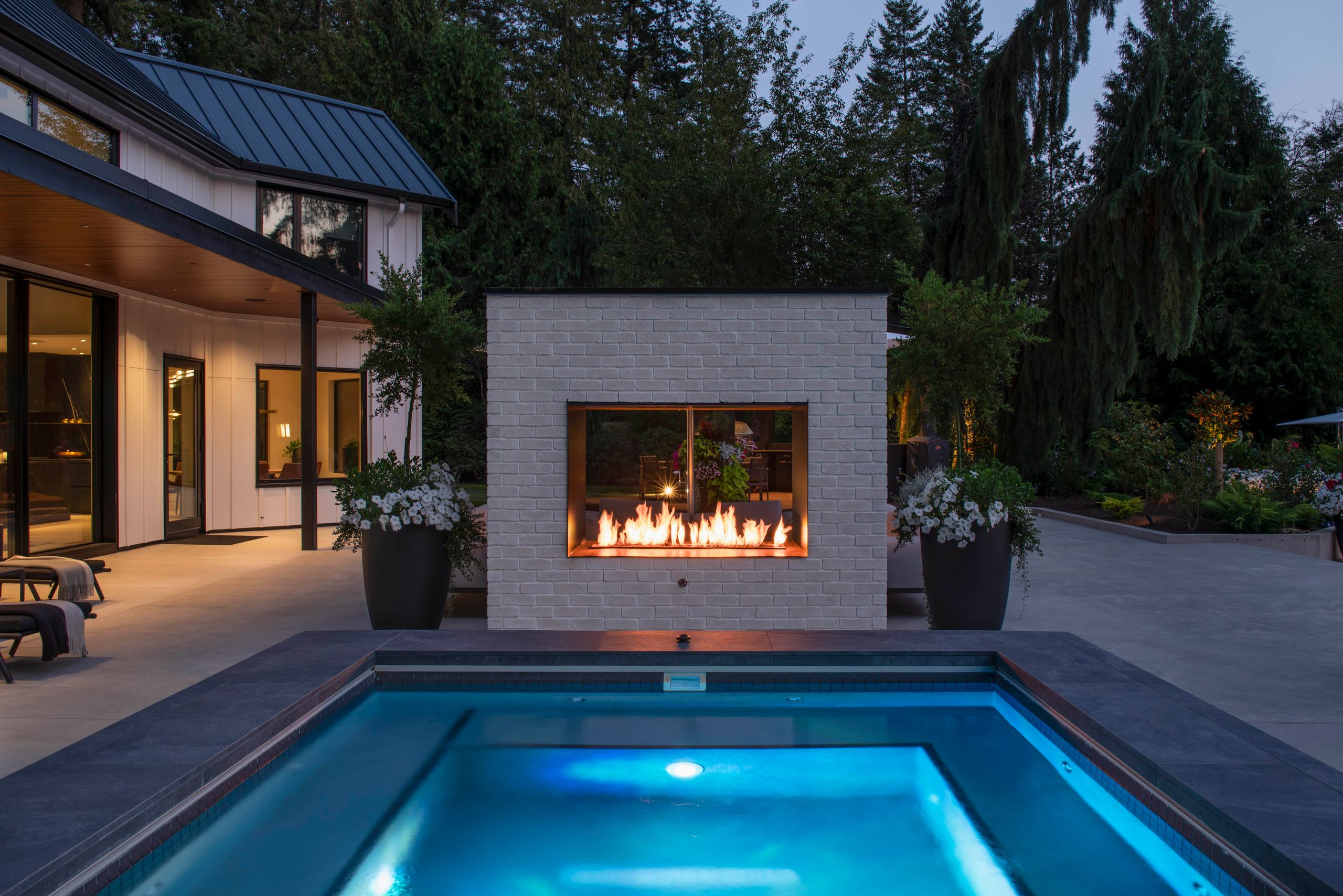 See-through gas fireplace in white brick dividing the pool from the terrace