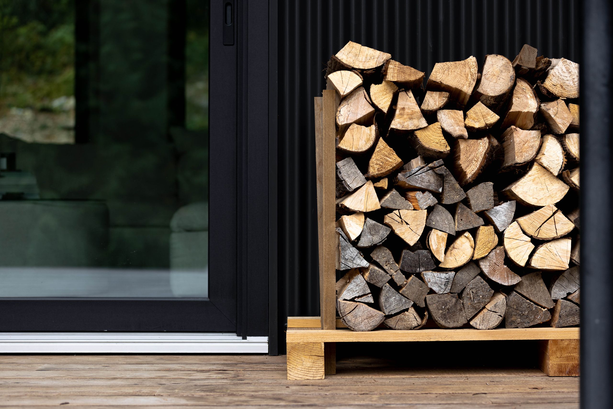 Stacked firewood in a cedar cradle against the black corrugated cladding