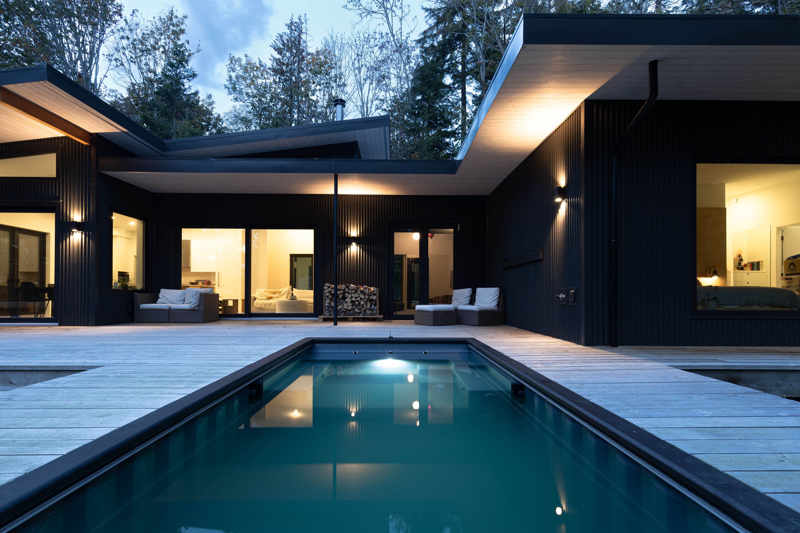Courtyard pool at dusk, reflecting the lit interiors of the black timber house